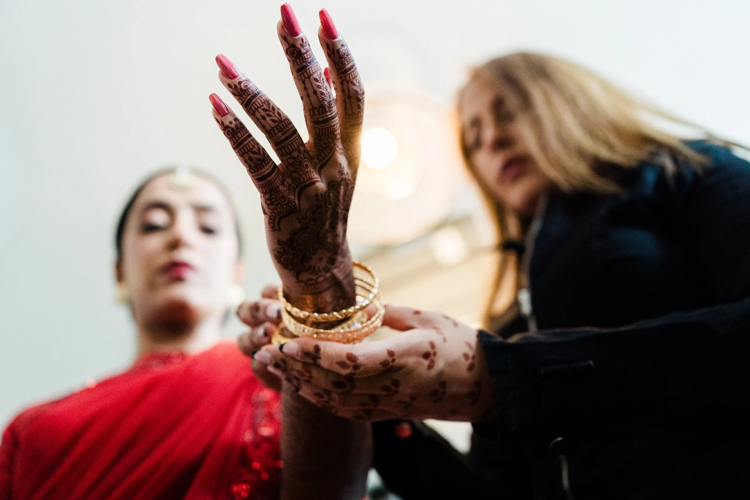 Two women with one showing her decorated hand and jewelry, dressed in traditional Indian attire.