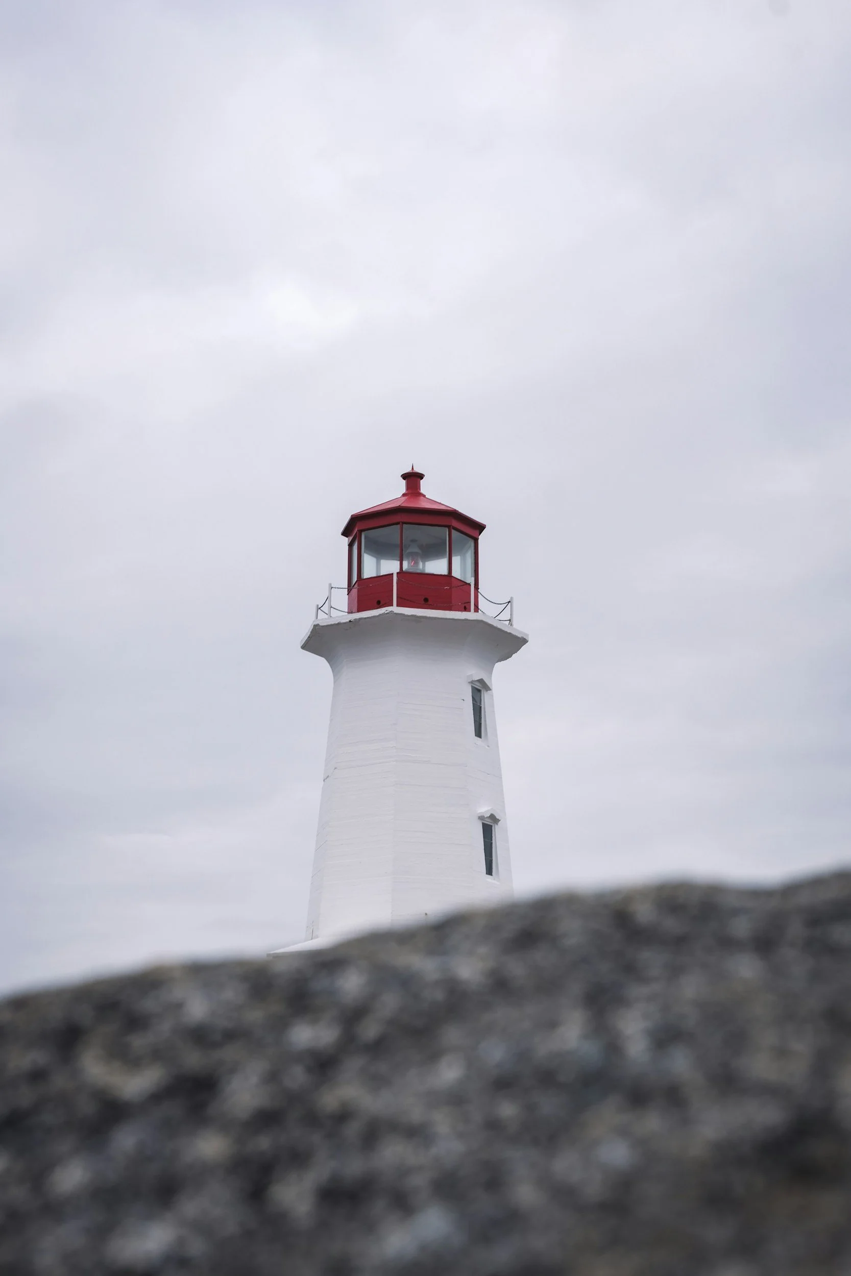 A white lighthouse with a red top against a cloudy sky, with a blurred dark foreground at the bottom.