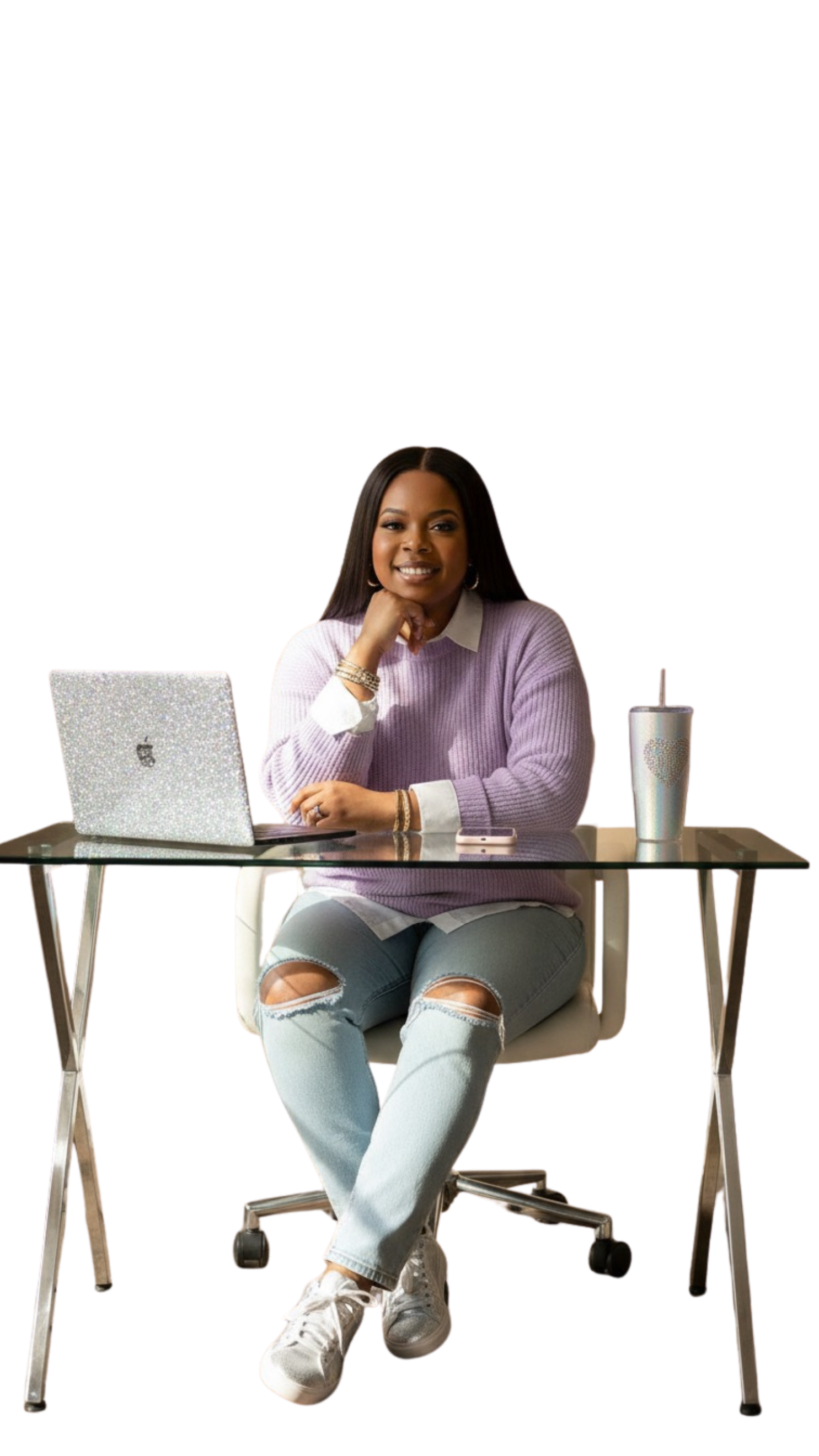 Young woman sitting at a desk with a laptop, coffee tumbler, and phone, smiling at the camera.