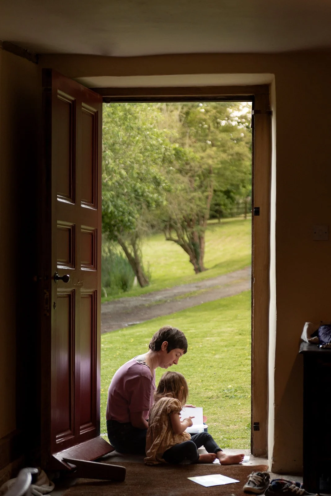 A woman and a child read a book in a doorway lit by afternoon light