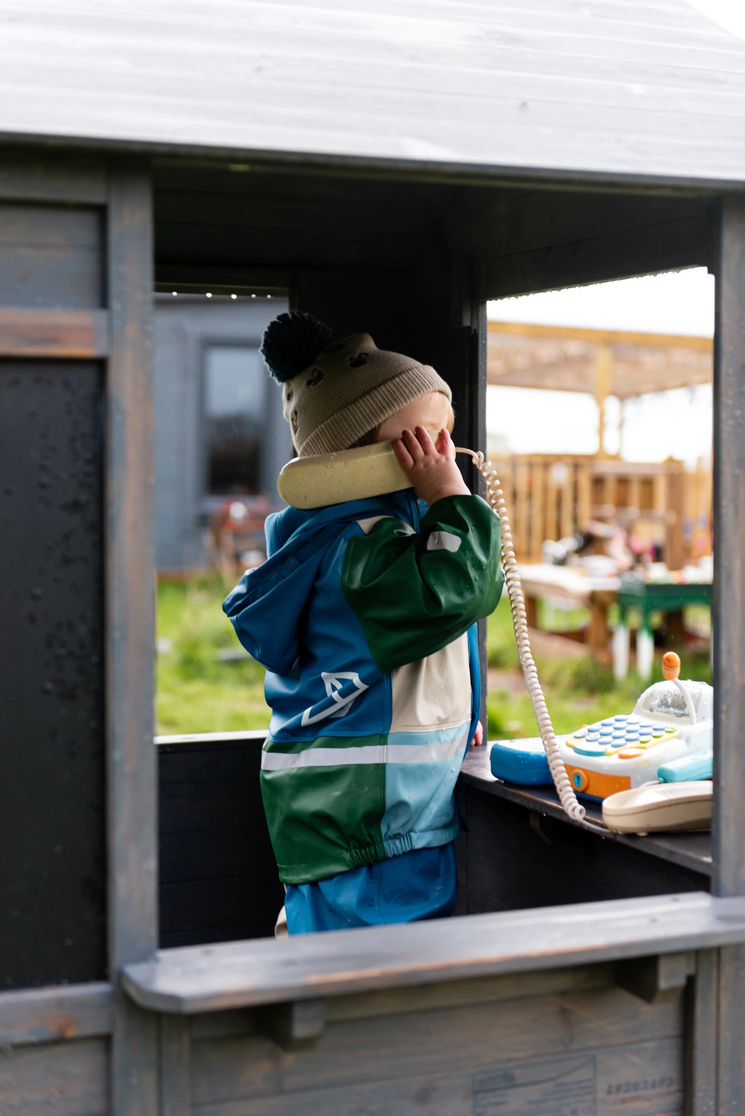 a small child in full waterproof gear holds a plastic toy phone against his face