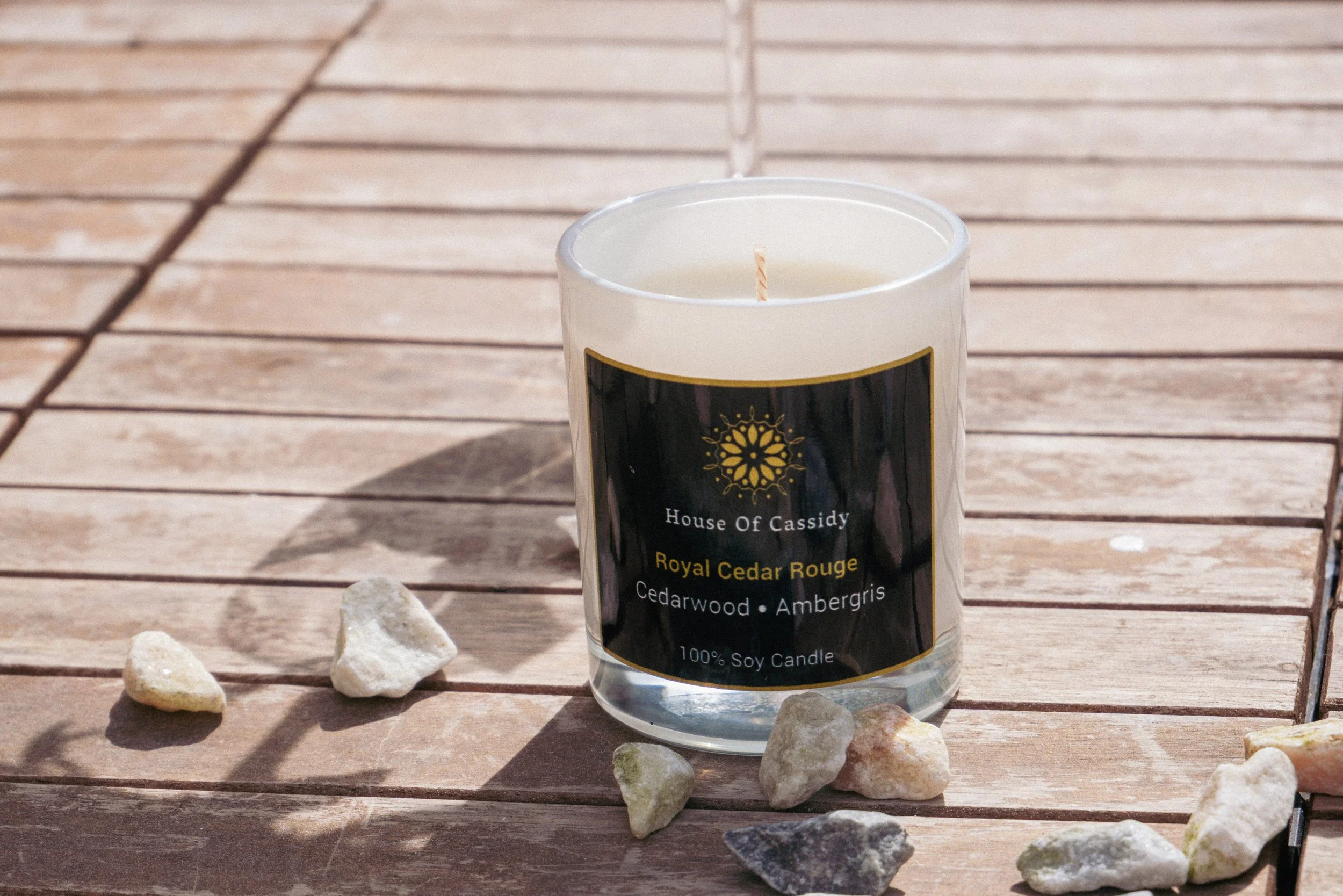 Royal Cedar Rouge candle on a wooden patio floor surrounded by rocks