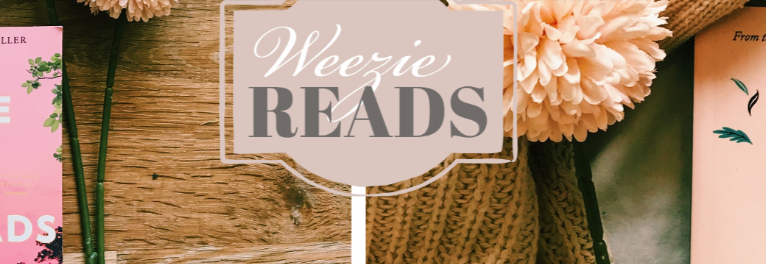 Sign with text 'Wezie Reads' on a wooden table surrounded by pink flowers and books.