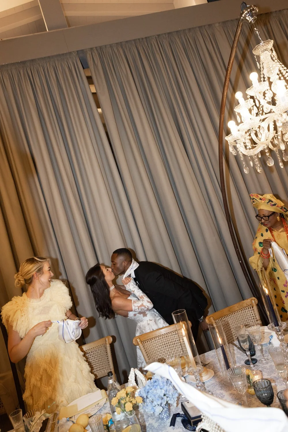 An intimate reception moment under a glowing chandelier, where emotion and elegance meet. A refined vision of a Podere Tesoro Tuscany luxury wedding dinner, captured with editorial depth and warmth