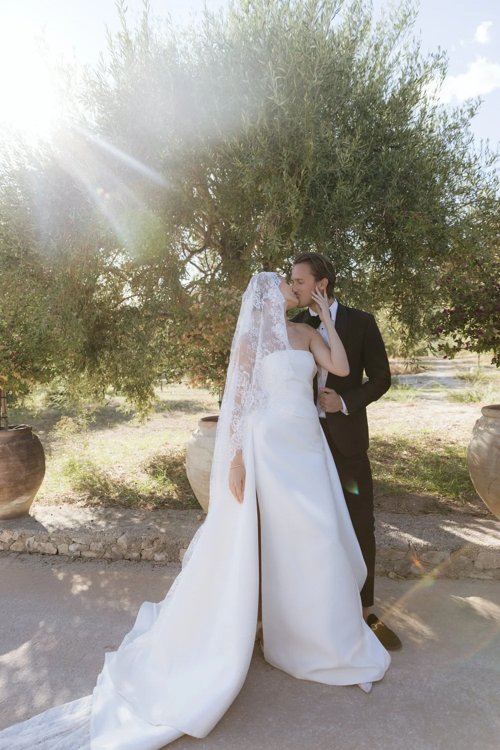 Sunlit bride and groom portrait under olive trees with a soft, candid kiss, reflecting the effortless beauty of a Braccialieri Sicily wedding and editorial destination wedding style