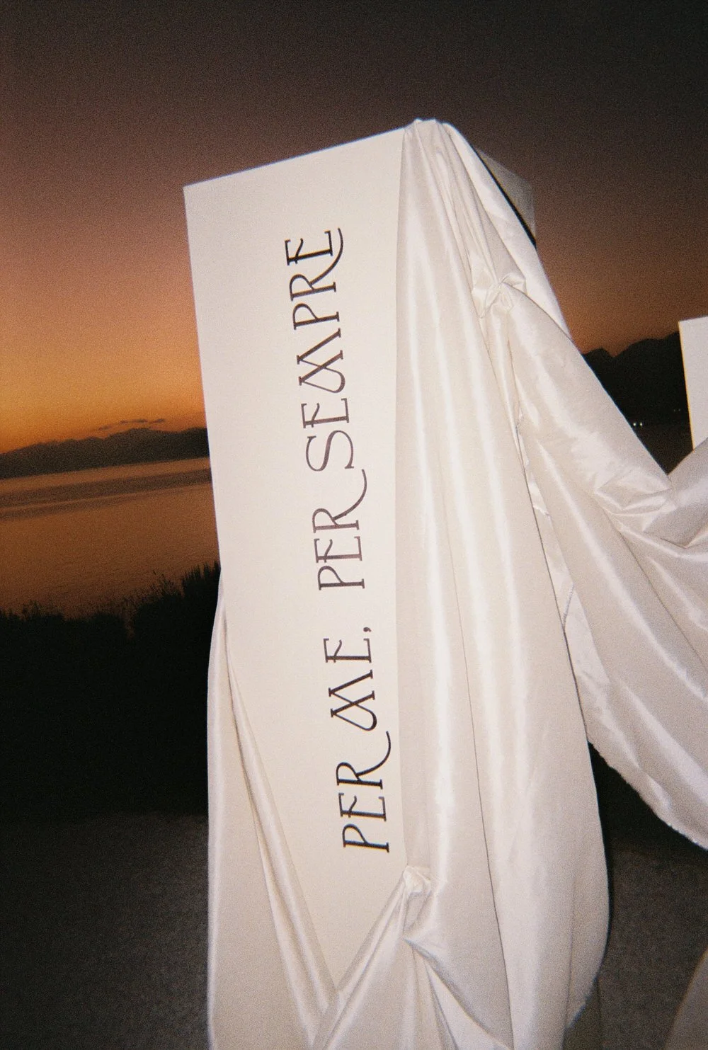 Sicily wedding film photography at sunset, featuring modern editorial signage with the phrase ‘Per Me, Per Sempre’ draped in silk, minimalist yet emotionally intentional design