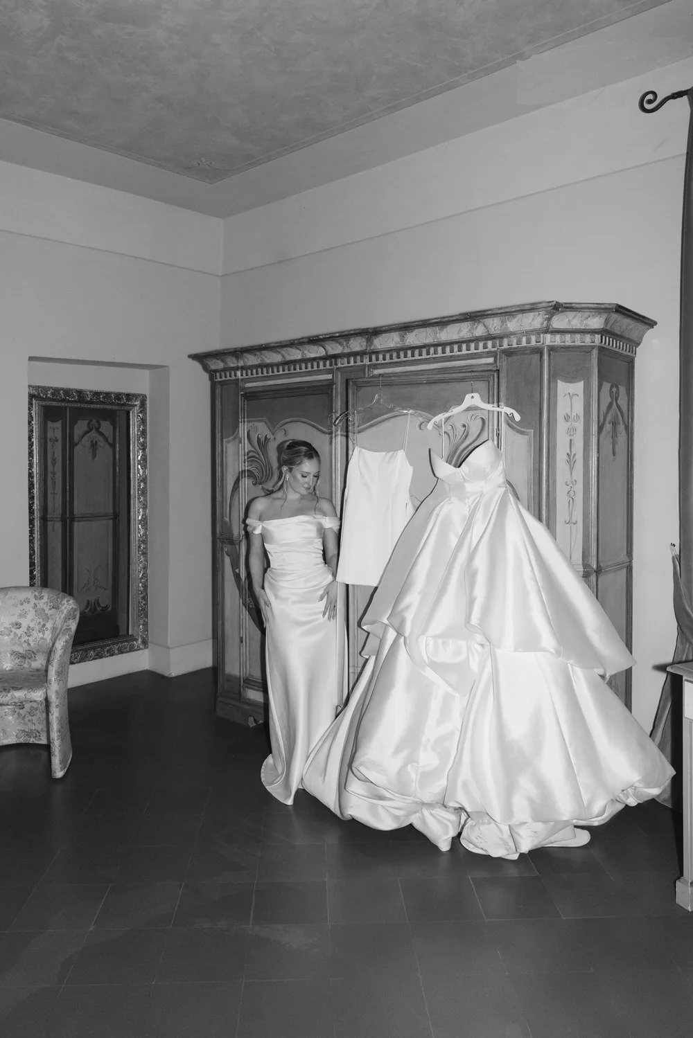Bride in a satin gown admiring her three Steven Khalil wedding dresses in a villa suite at Villa La Palagina in Tuscany. Captured in timeless black and white, the scene evokes editorial elegance and intentional bridal styling
