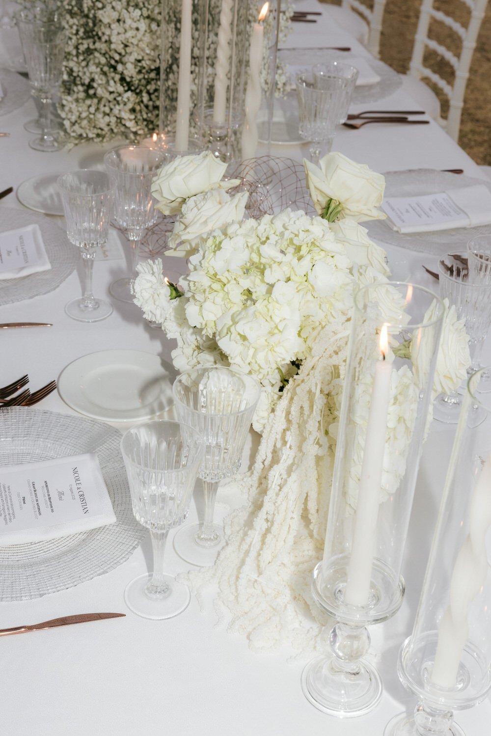 Elegant white floral centerpiece with roses and hydrangeas, crystal glassware, candles, and fine table settings at a Commenda San Calogero wedding reception in Sicily, showcasing refined modern styling and minimalistic luxury