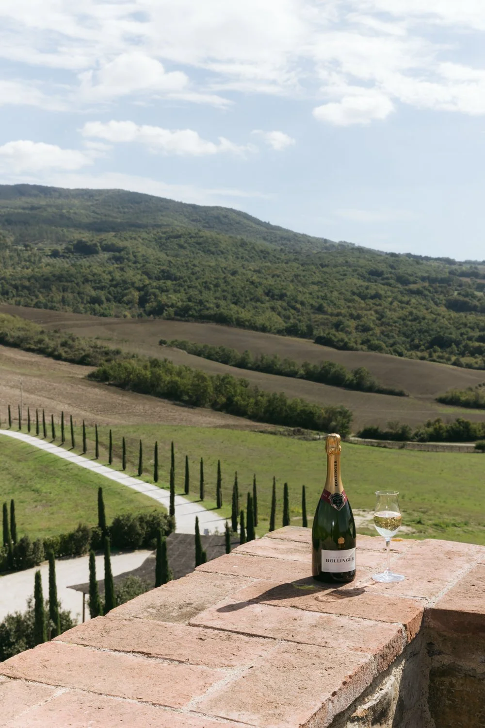 podere tesoro tuscany wedding overlooking rolling Tuscan hills with champagne on a stone terrace. A luxury destination wedding setting in Tuscany, Italy featuring cypress-lined roads, vineyard views, and timeless countryside elegance
