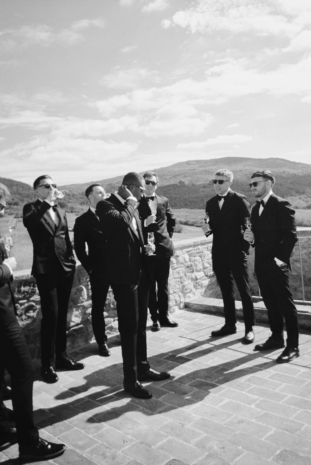 podere tesoro tuscany wedding black and white groomsmen portrait captured on 35mm film on a Tuscan terrace with champagne. Timeless, editorial groom style inspiration for a luxury wedding in Tuscany, Italy