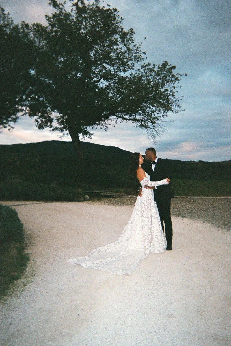 Bride and groom embrace under a large tree at sunset on a gravel path at Podere Tesoro, captured on 35mm film. A timeless, classic portrait from a Podere Tesoro Tuscany wedding