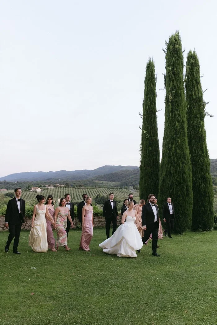 Wedding party walking through the cypress-lined gardens at La Palagina in Tuscany, captured with natural light and refined elegance during a destination wedding celebration