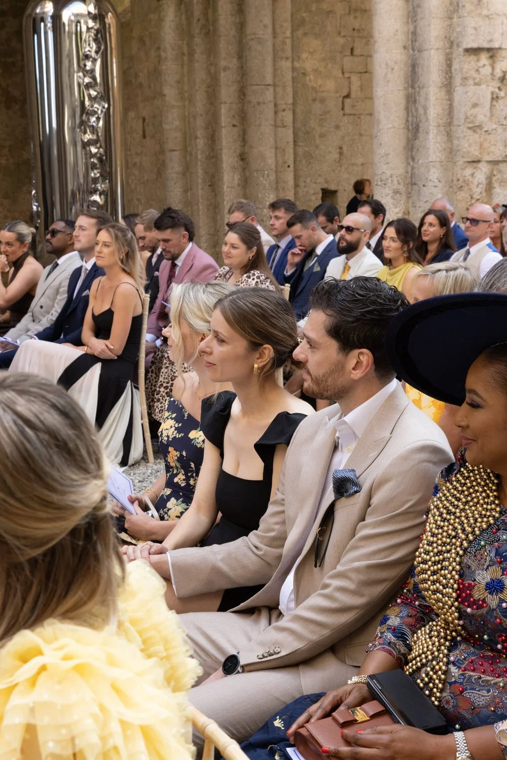 Guests sit immersed in a quiet, emotional ceremony within historic stone walls. A sophisticated San Galgano Abbey wedding scene capturing presence, elegance, and atmosphere
