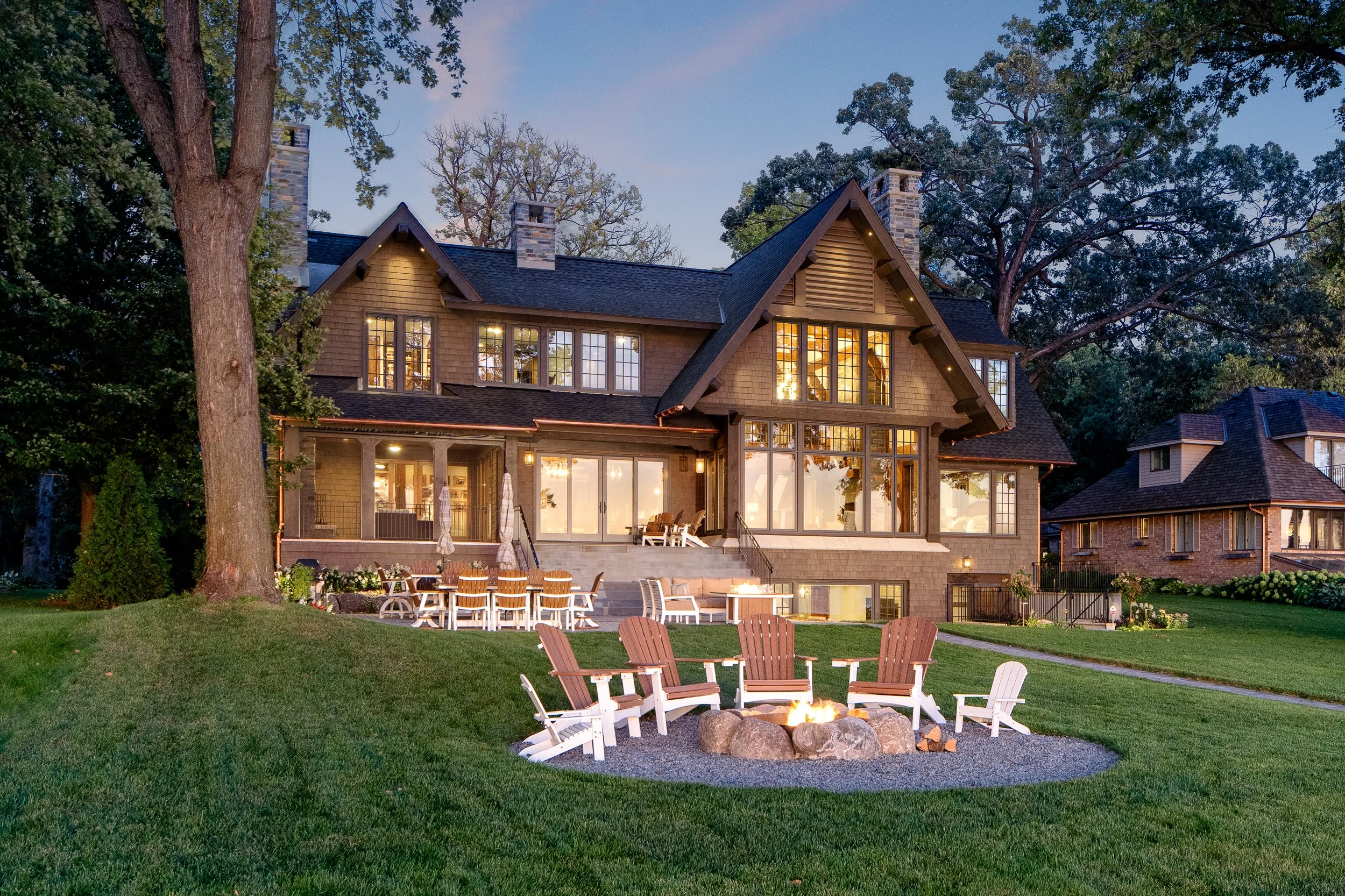 Outdoor fire pit with Adirondack chairs behind Craftsman-style home