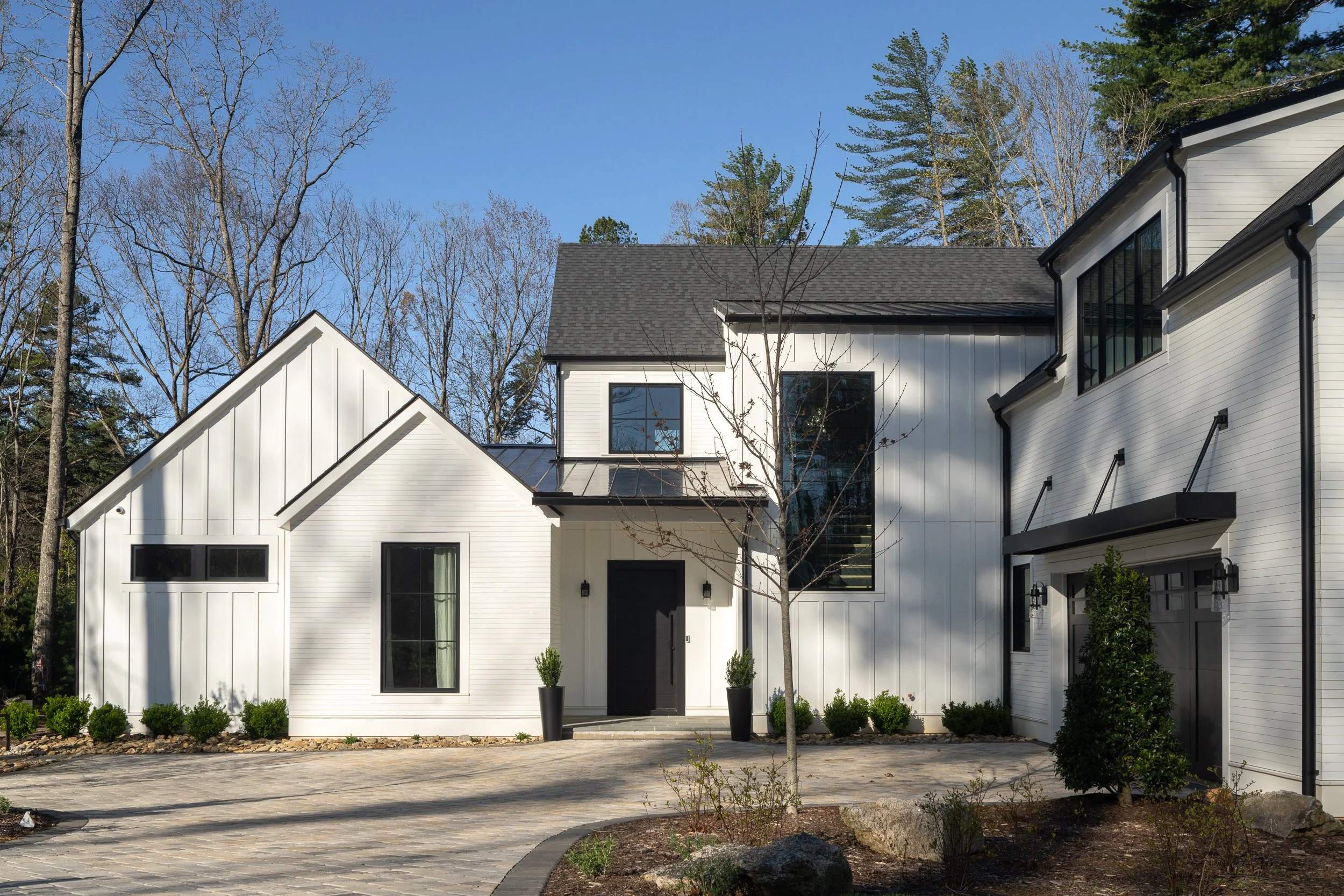 Front view of a modern white farmhouse with black accents and a spacious driveway.