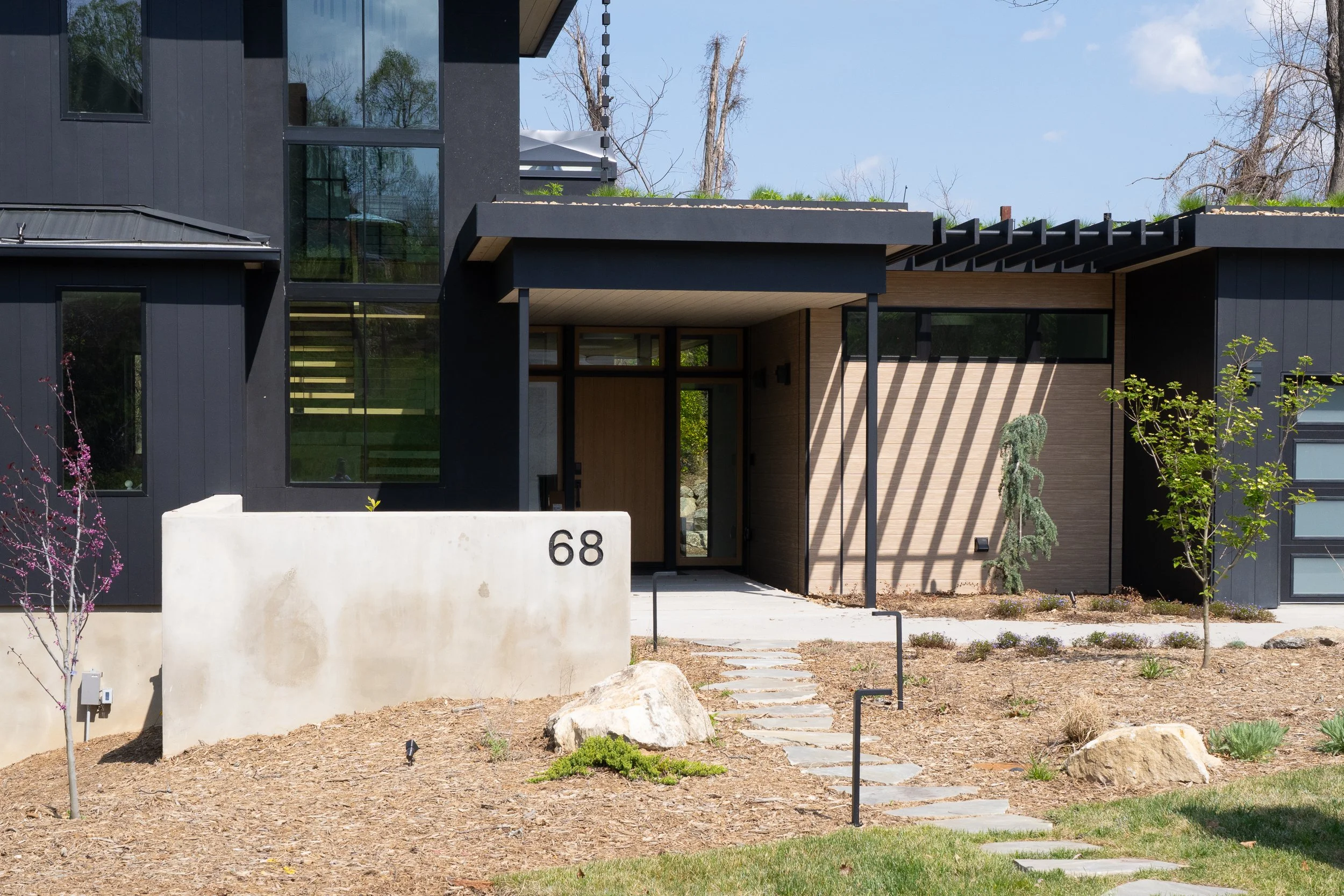 Entry approach with stone pavers, concrete address wall, black exterior cladding, and covered doorway.