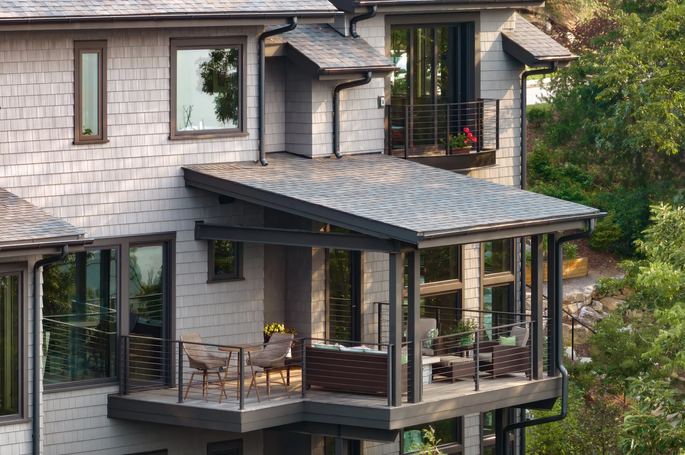 Contemporary home with glass railing balcony and shaded outdoor seating.