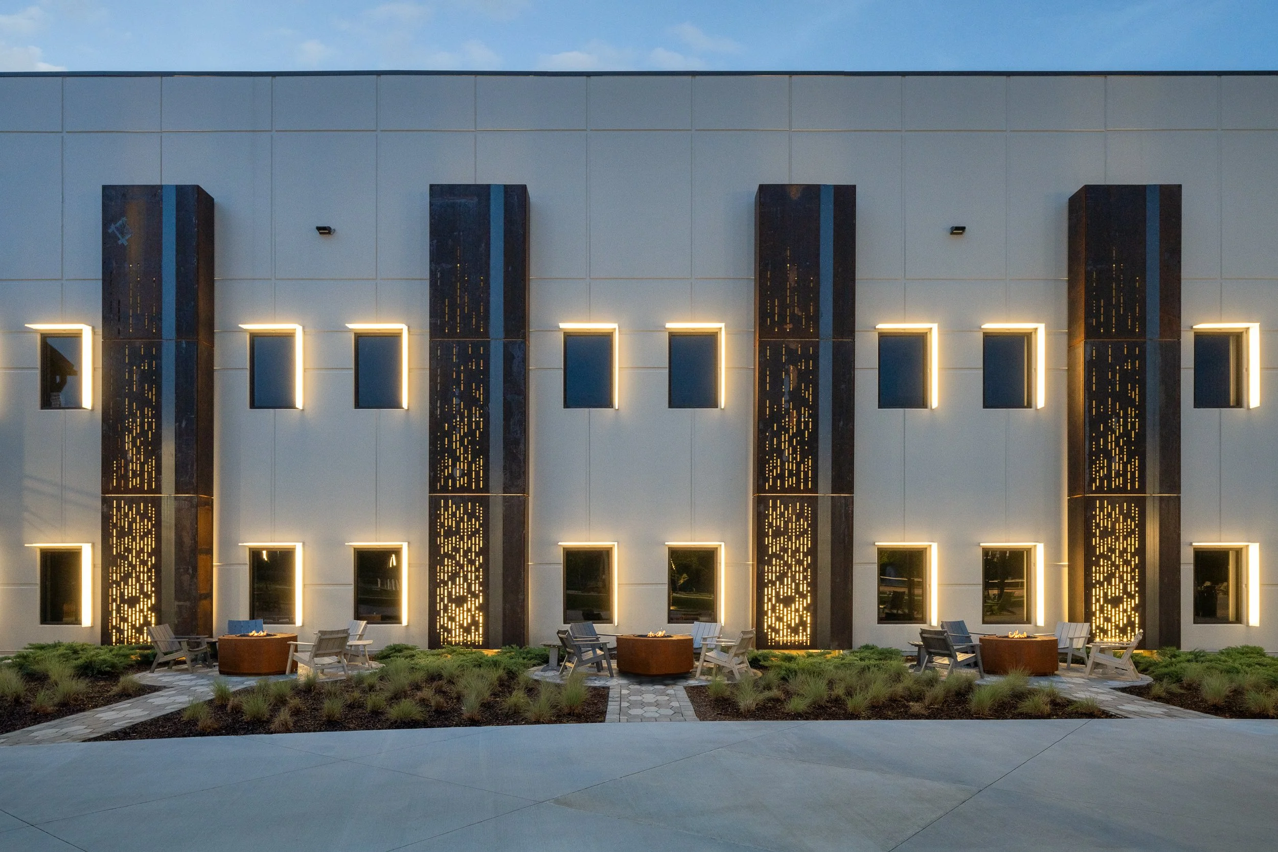 Contemporary building facade with vertical illuminated panels and seating area.
