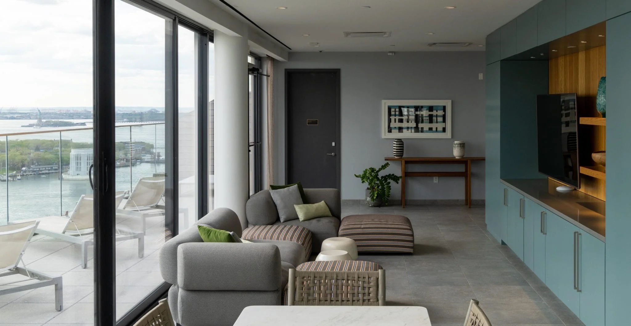 High-rise amenity lounge with soft seating, blue built-in cabinetry, floor-to-ceiling glass, and a terrace overlooking the water.
