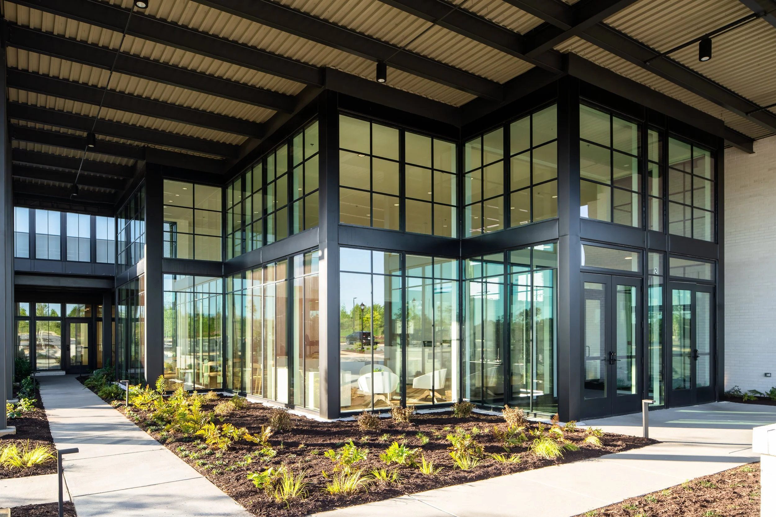 Industrial-modern entrance with black steel beams and landscaped pathways.
