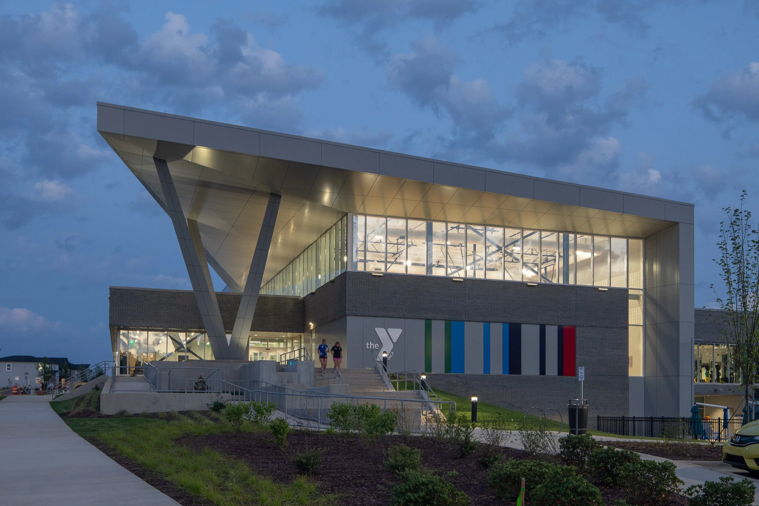 Chatham Park YMCA illuminated at twilight with glowing fitness spaces, entry ramp and colorful facade accents.