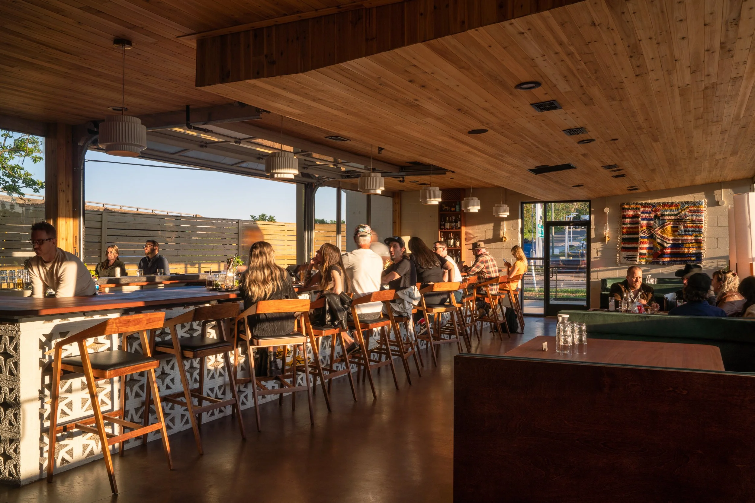 Guests enjoying drinks at a stylish bar with warm wooden tones and pendant lights.