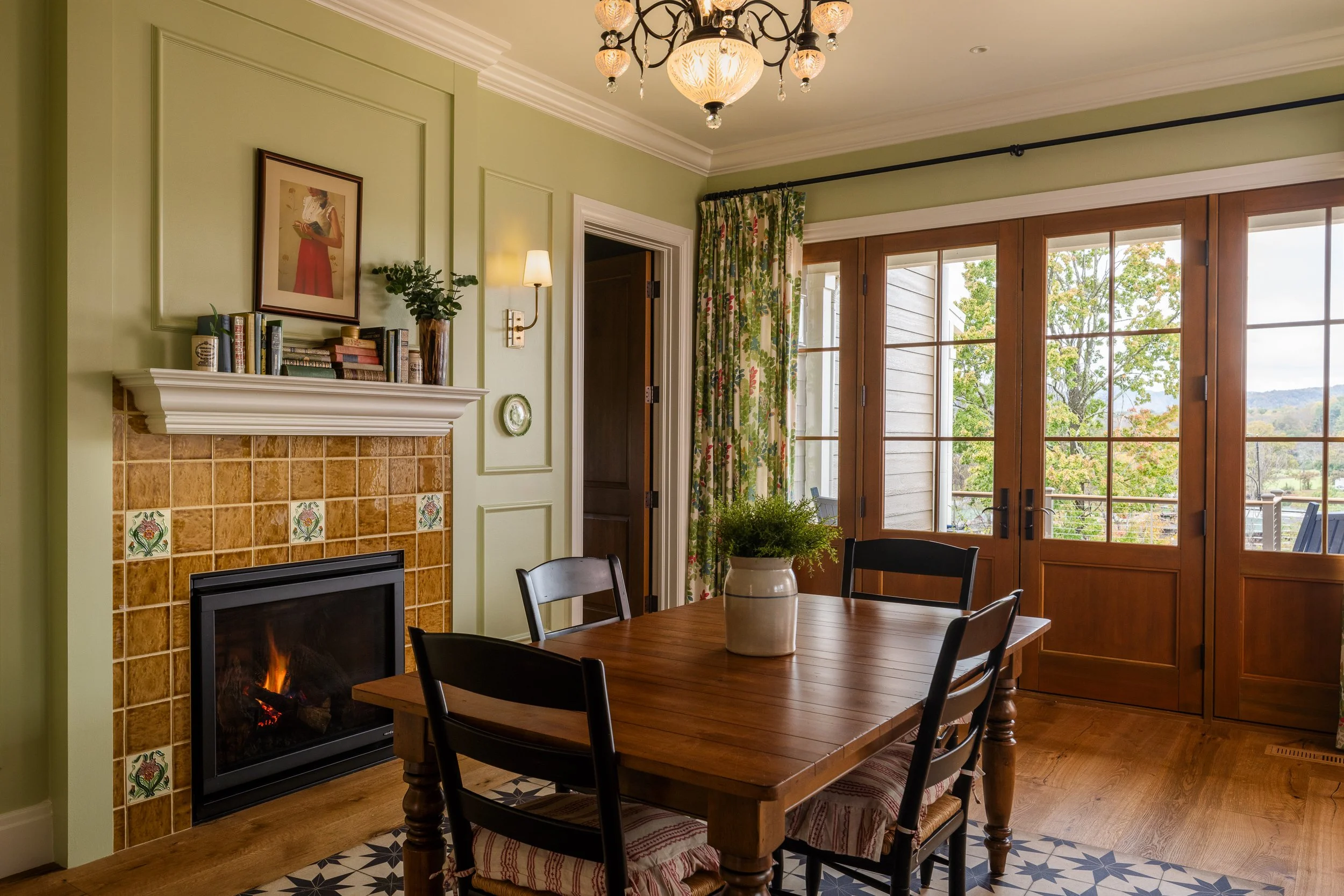 Green dining room with tiled fireplace, wood table, French doors, and soft natural light