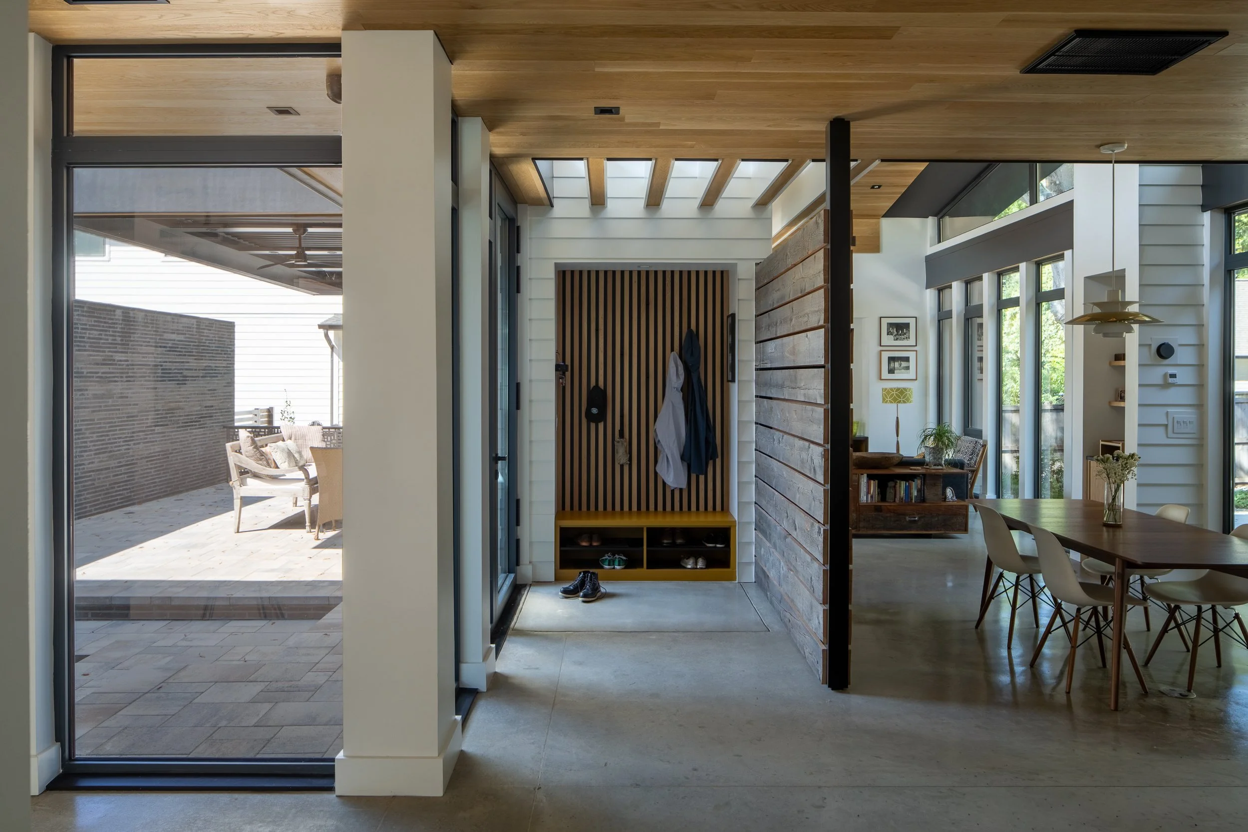 A polished gray floor connects courtyard windows, a recessed entry with vertical wood slats, and the adjoining dining area.