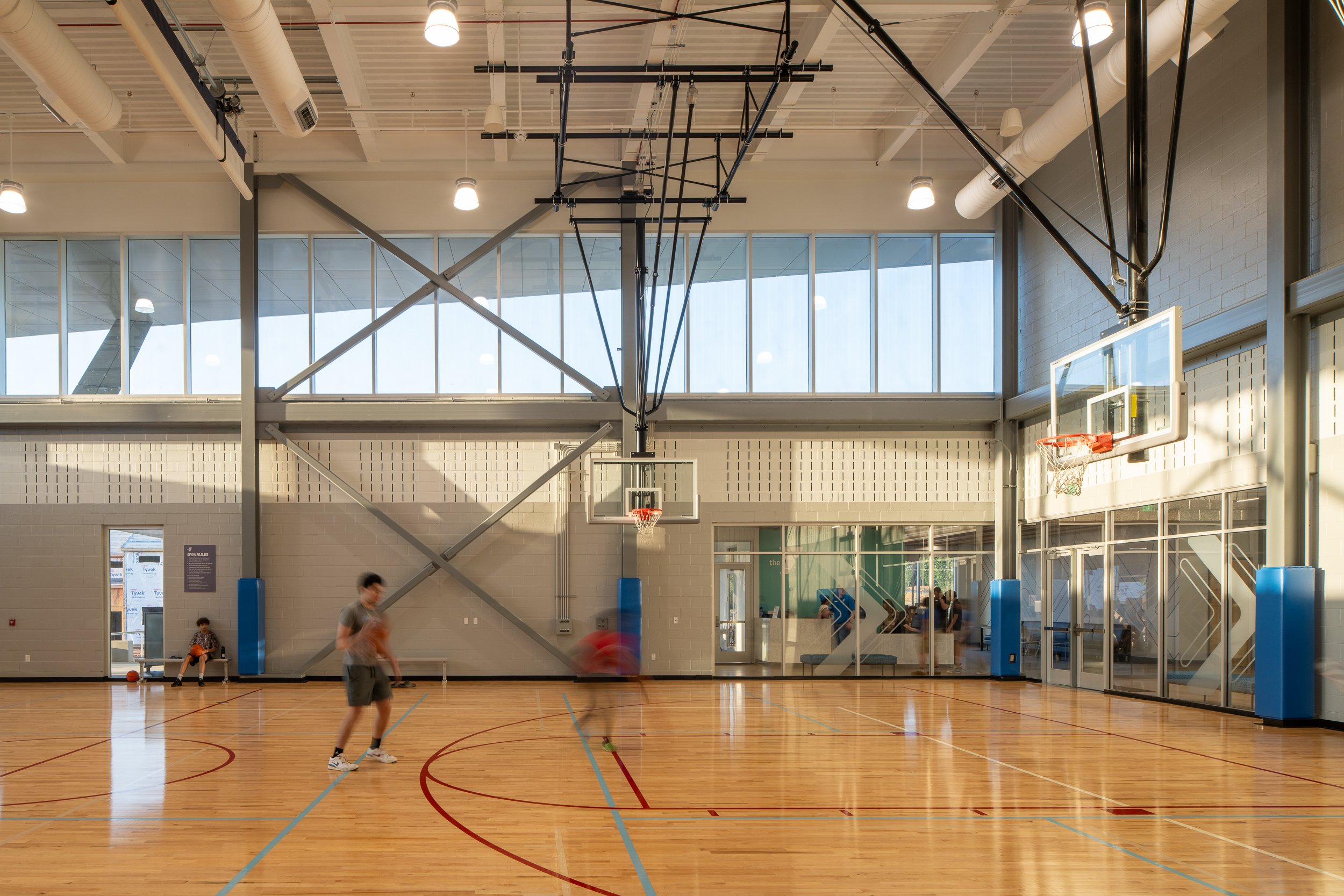 Indoor basketball court with high ceilings, large windows, and players moving across the gym floor.