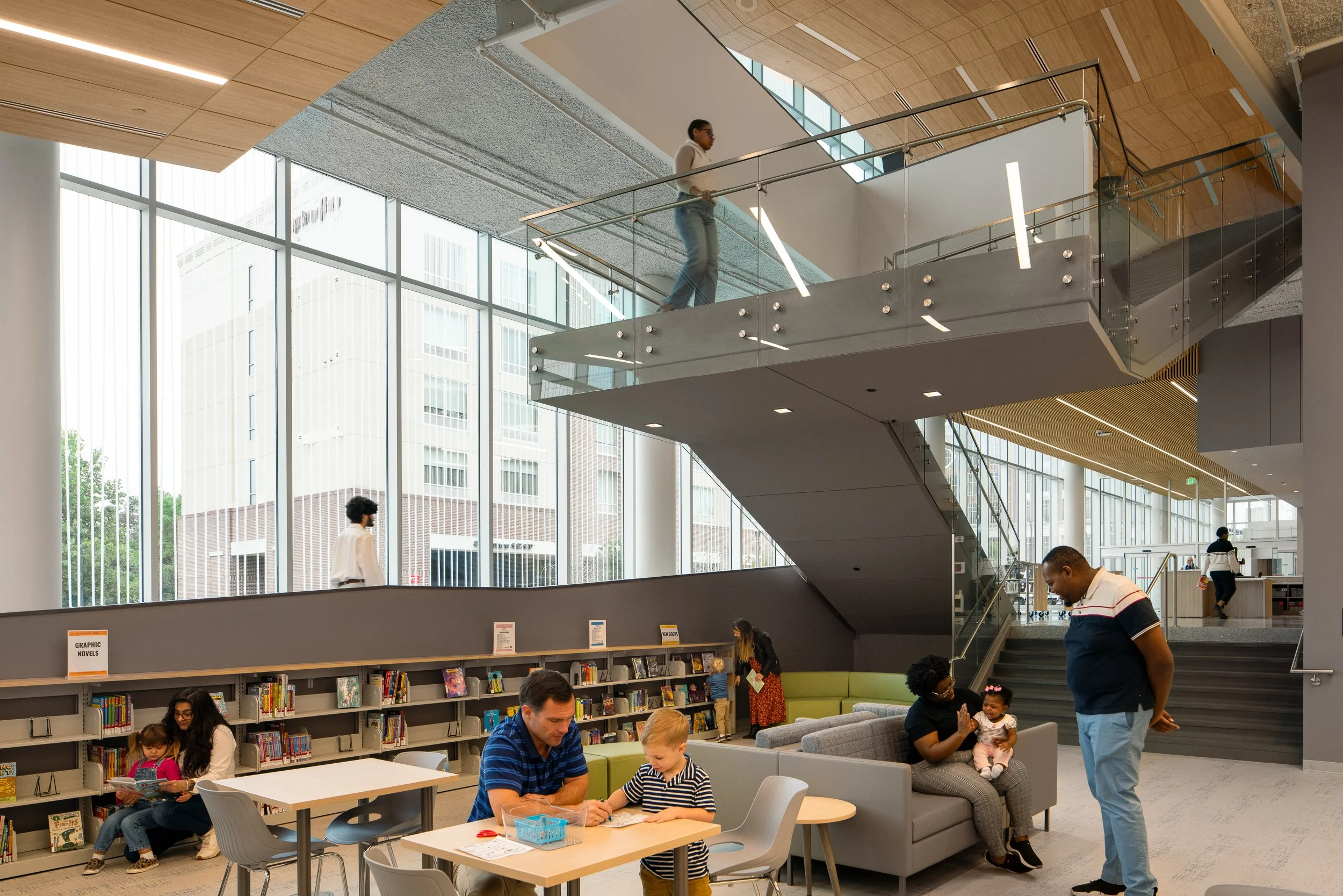 Children’s library area with bookshelves, family seating, glass railings, and central stair.