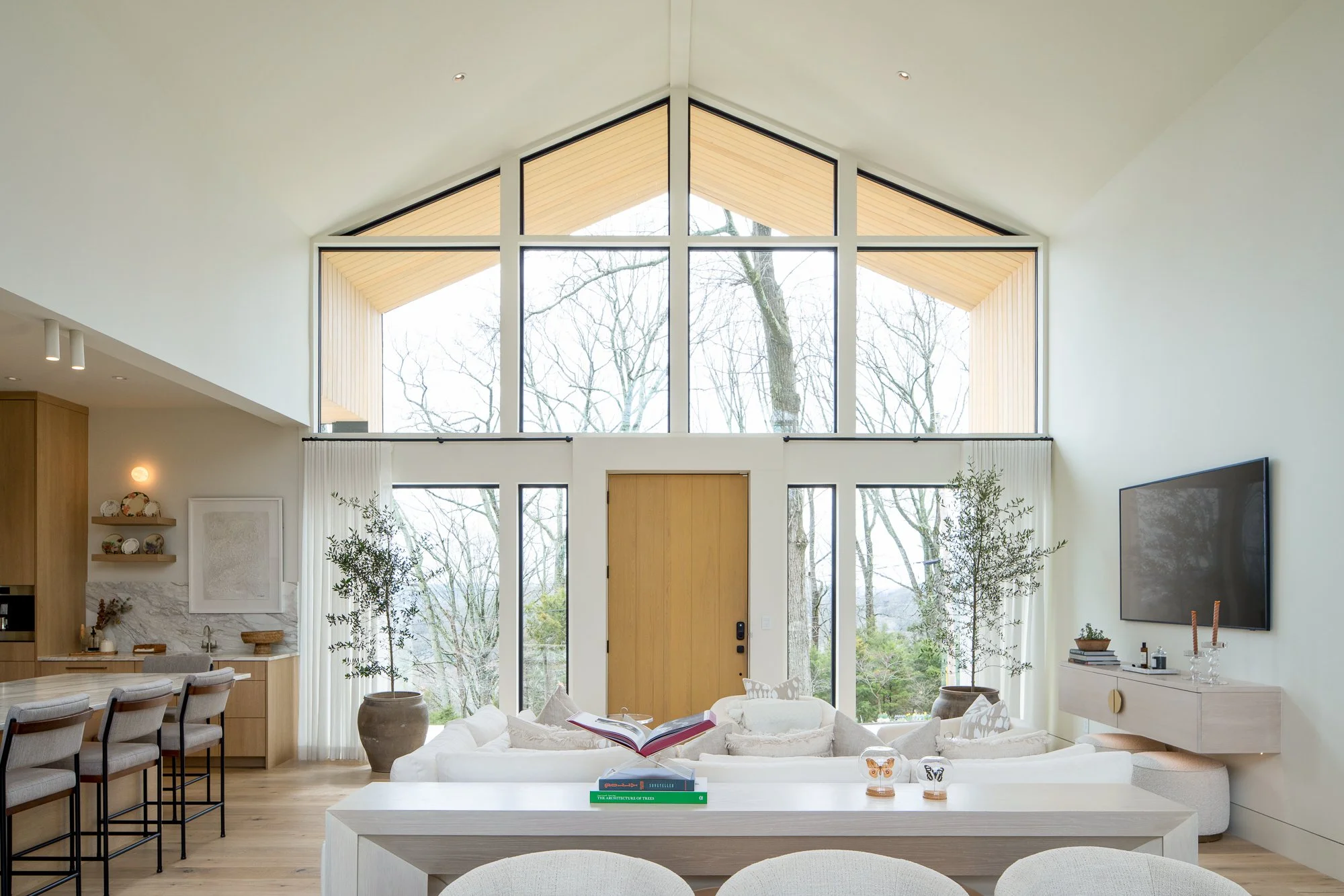 Double-height living room with gabled window wall, light wood ceiling, and front door.