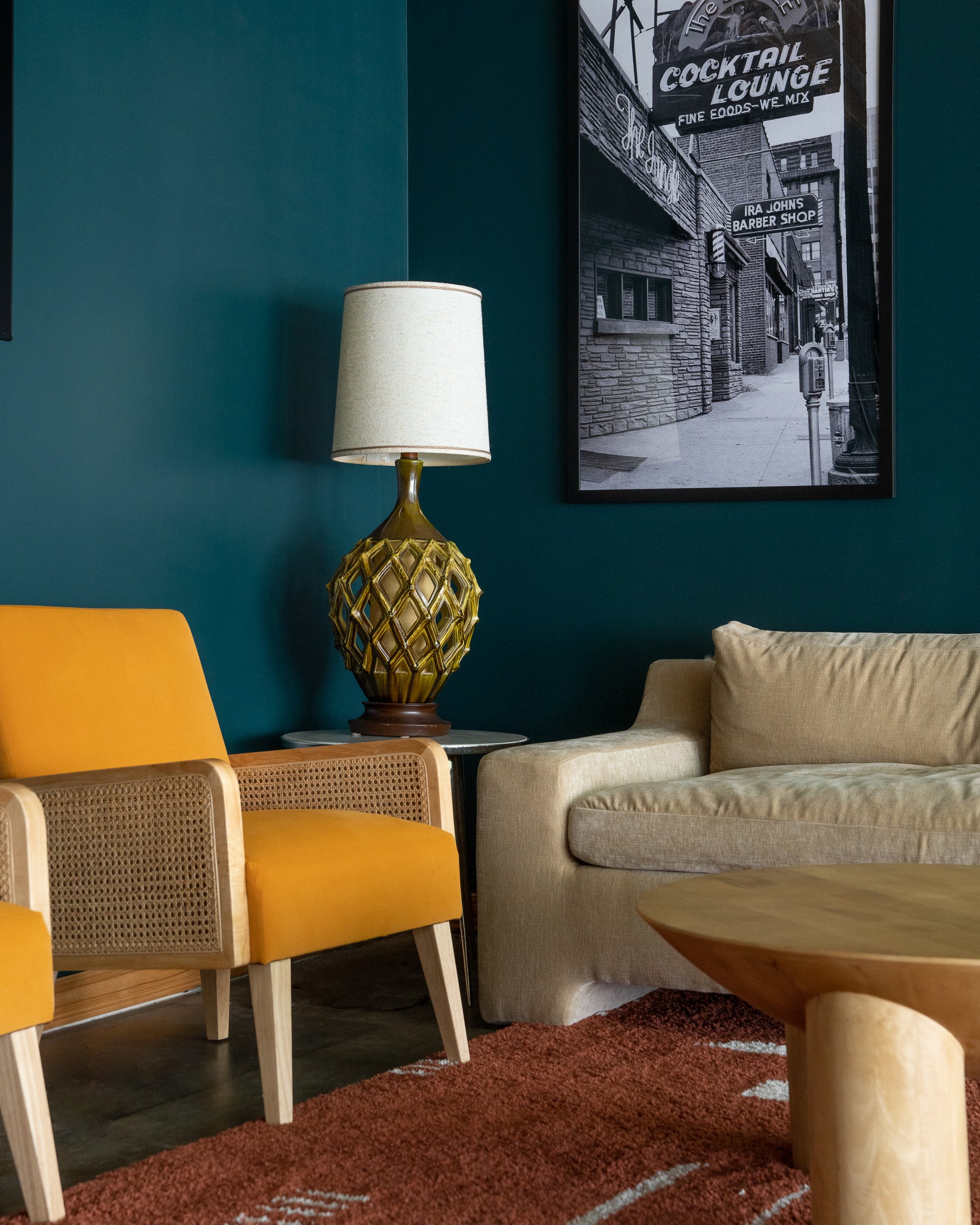 Close-up of mustard rattan chair, vintage lamp, and framed black-and-white cocktail lounge print.