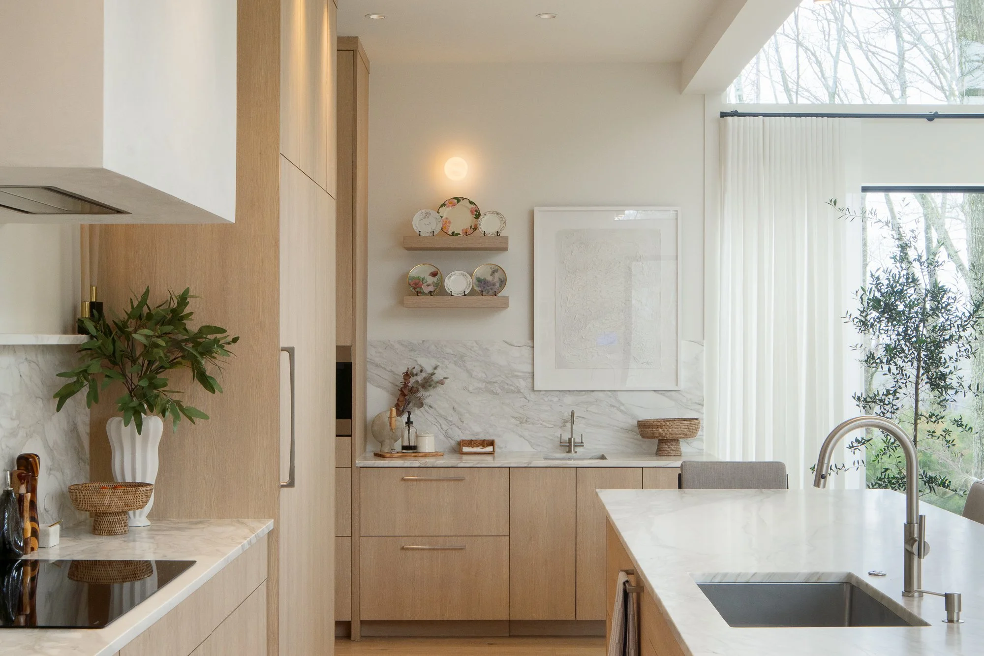 Light wood kitchen with marble backsplash, white island, and large window with curtains.