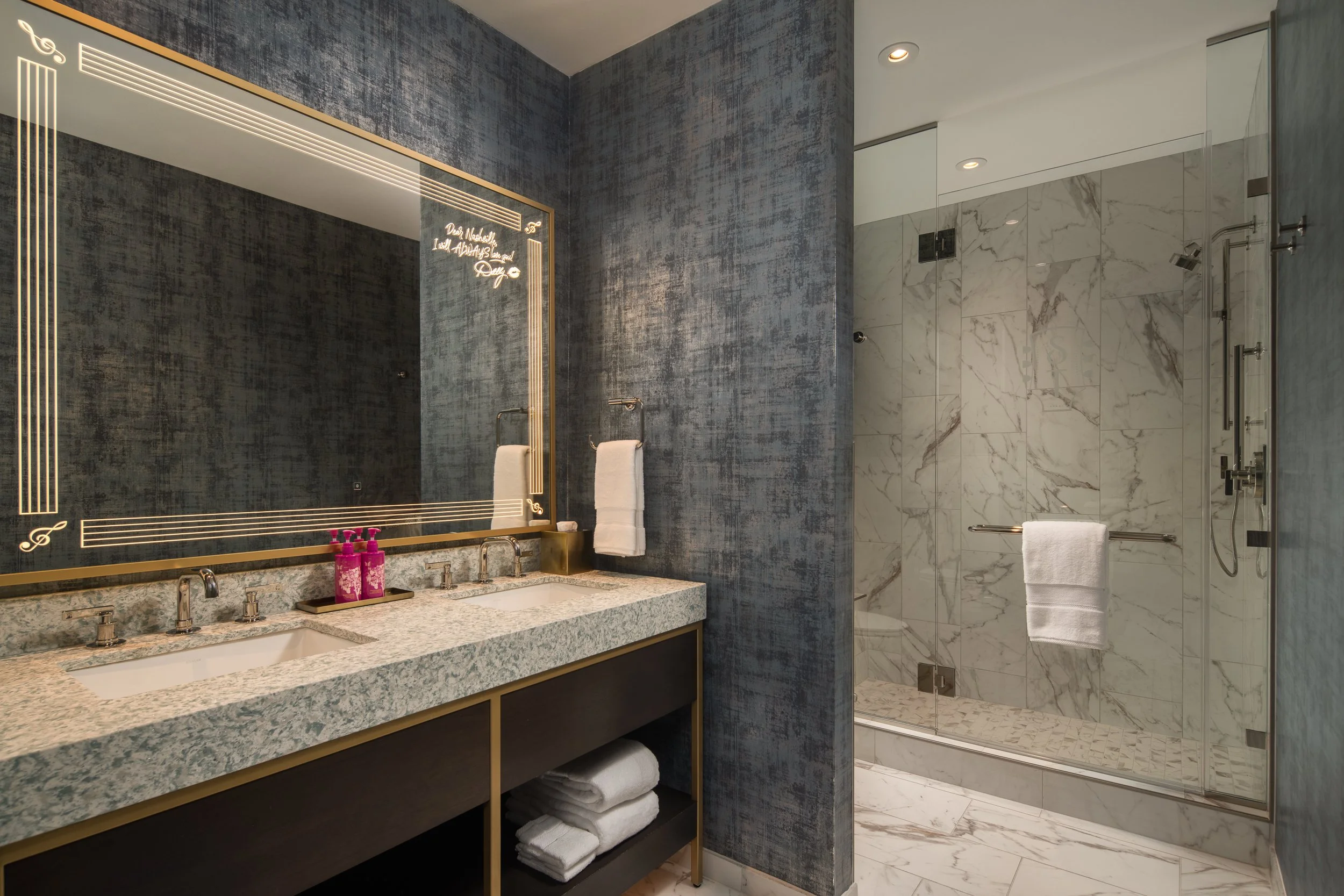 A sophisticated bathroom with accents of gold a musical motifs engraved into the mirror at the SongTeller Hotel in Nashvhille