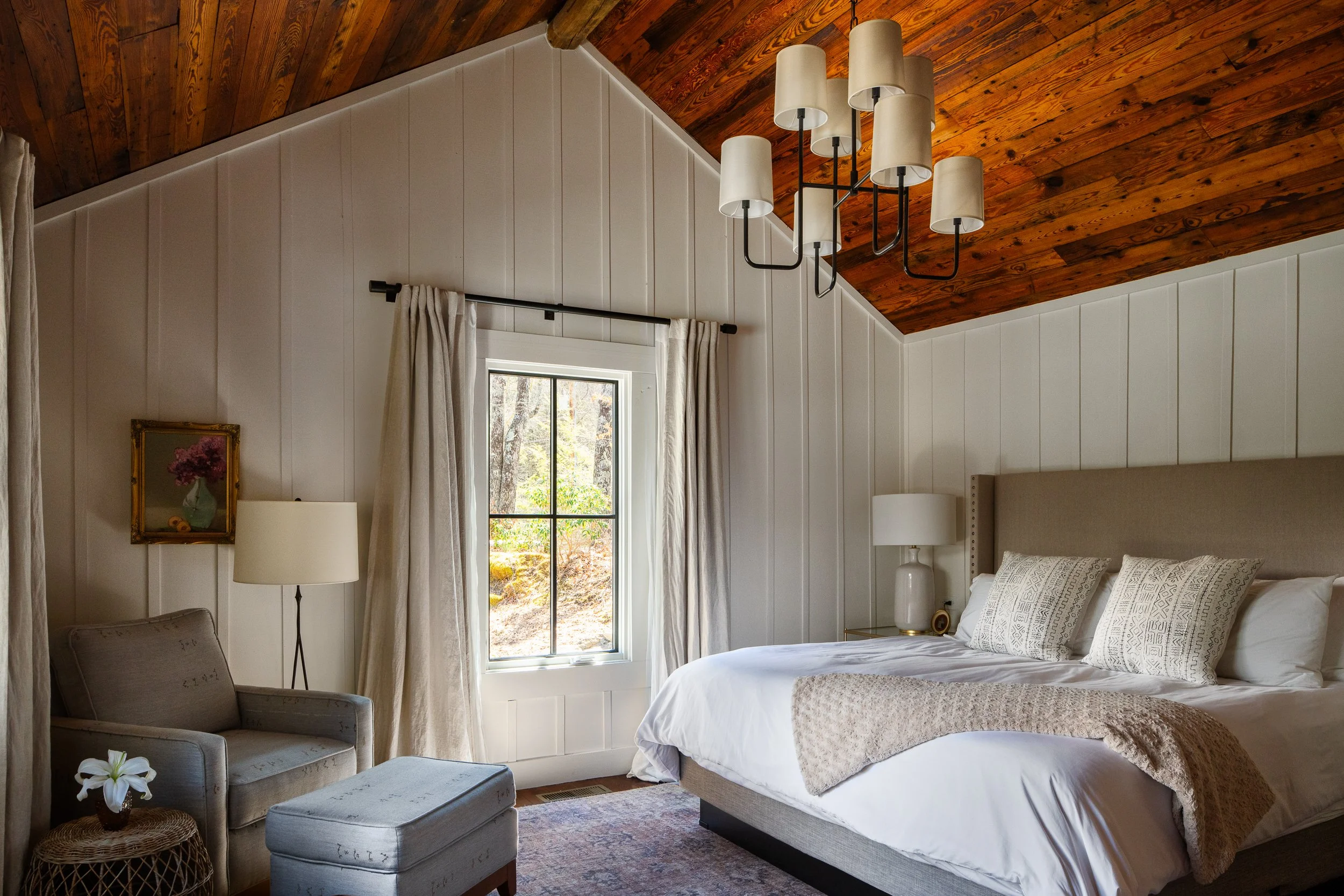 Bedroom with a vaulted wood ceiling, white paneled walls, upholstered bed, and soft neutral furnishings.
