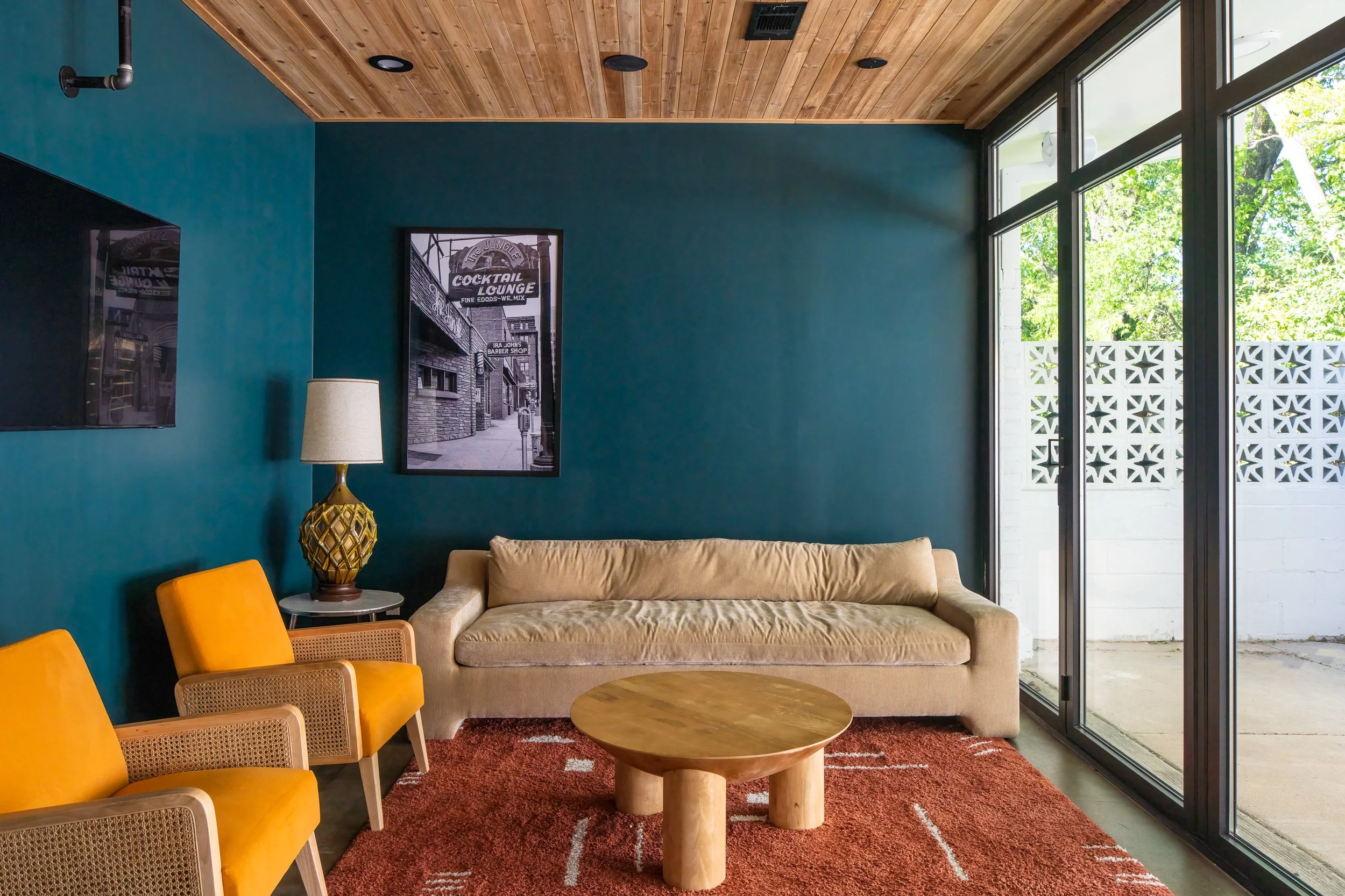 Seating area with teal accent wall, vintage artwork, mustard chairs, and a beige sofa.