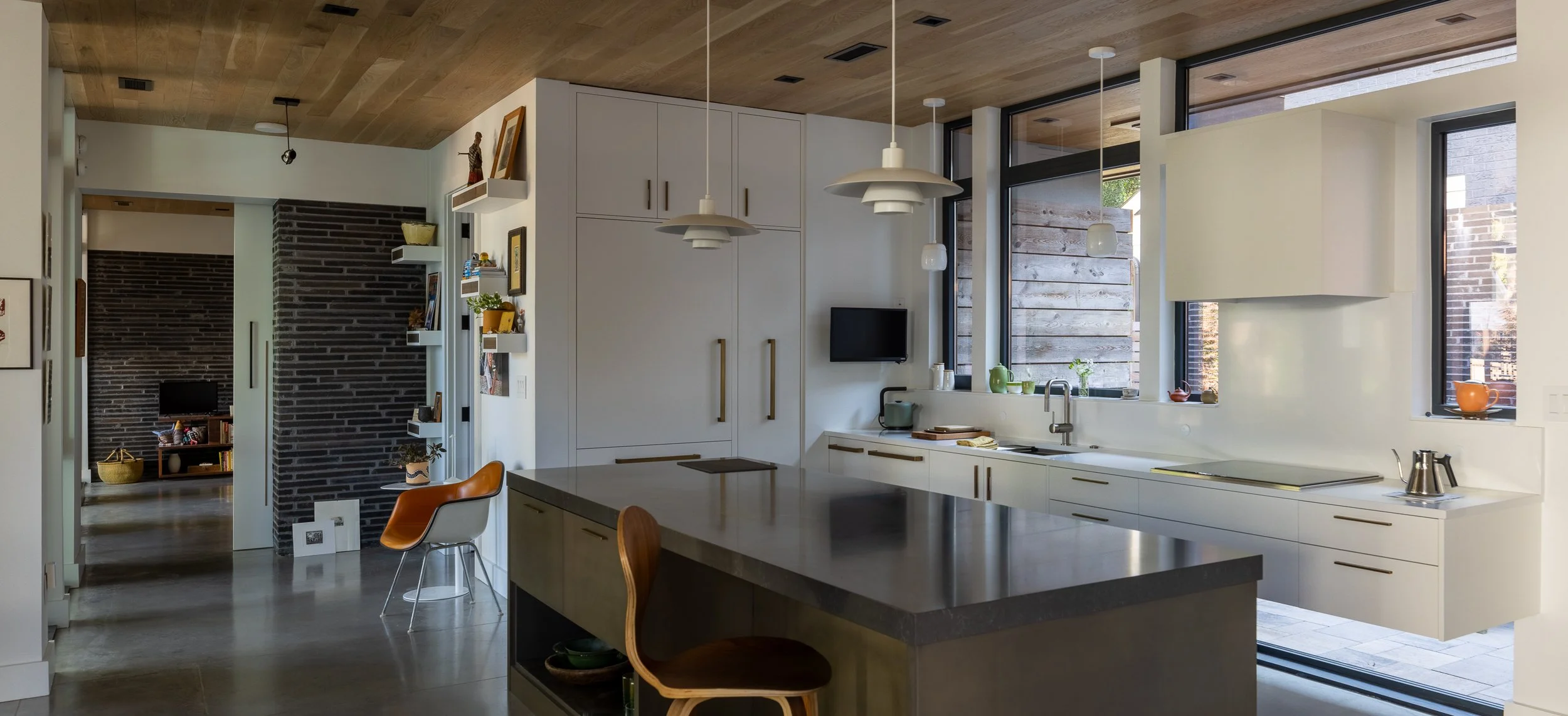 White kitchen cabinetry and a dark island frame a view toward the bedroom, with a wood ceiling and polished gray floor.