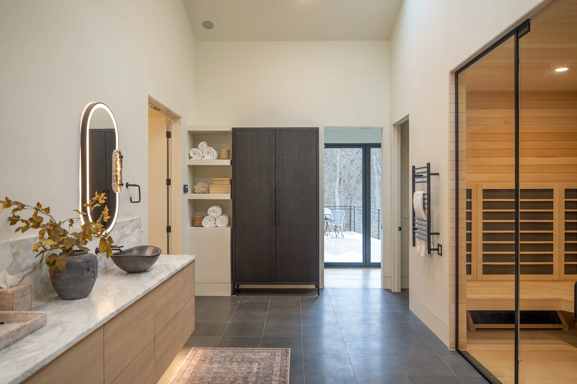 Spa bathroom with floating vanity, dark tile floor, and sauna behind glass.