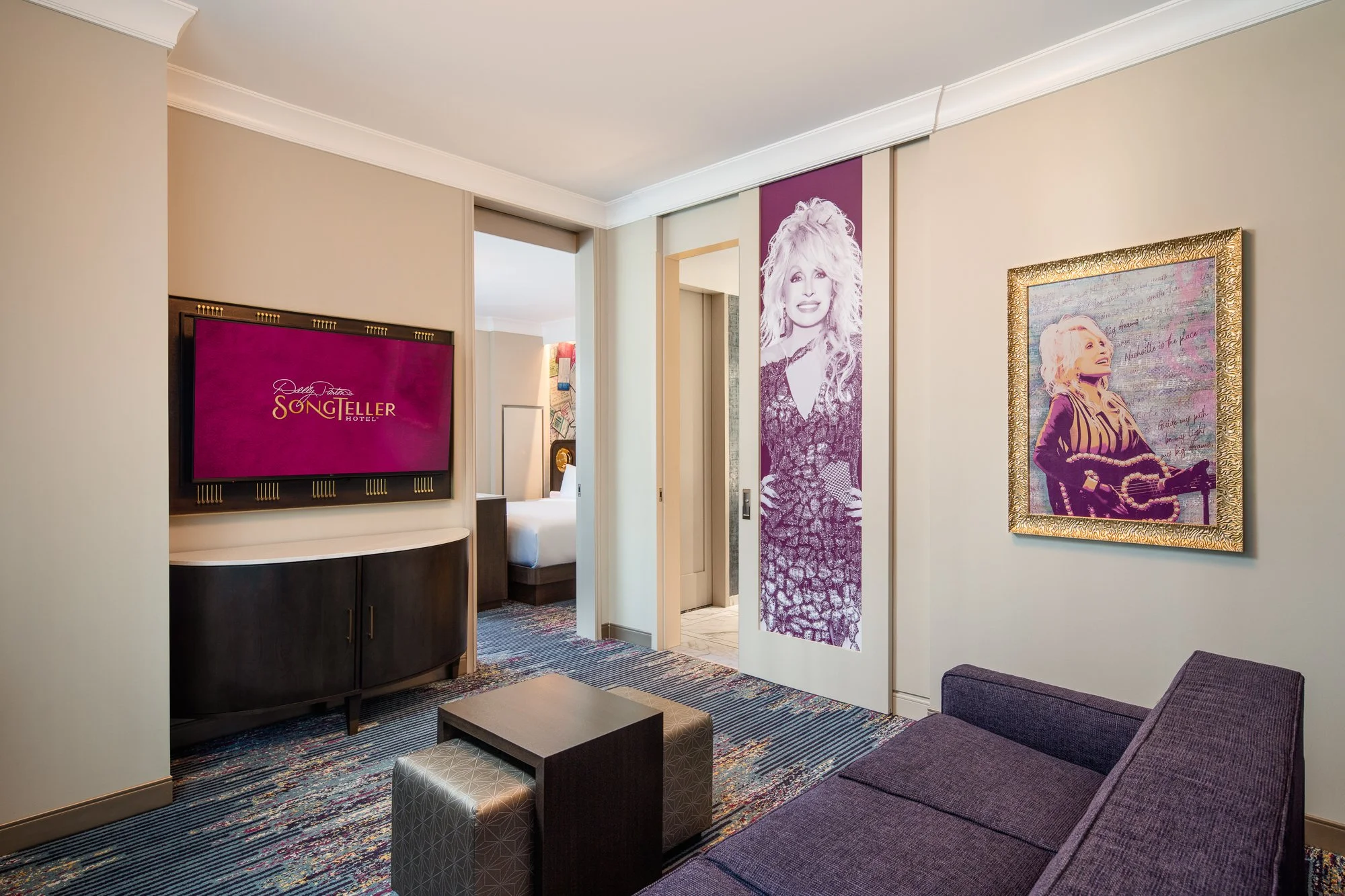 Living area inside a SongTeller Hotel suite with a purple sofa, custom television surround, Dolly Parton artwork, and sliding bedroom doors.