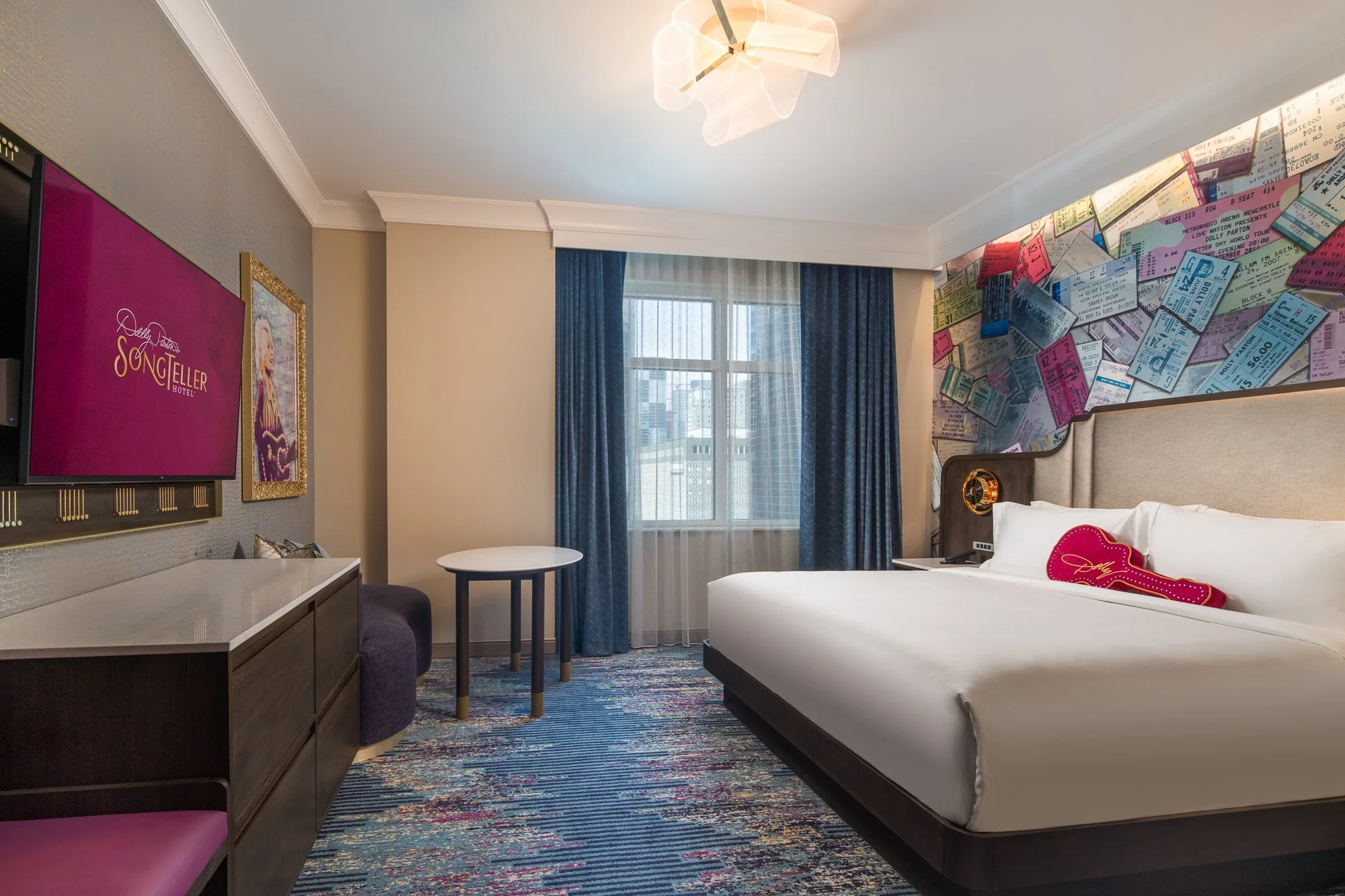 Nashville hotel guest room with a colorful concert-ticket mural, upholstered bed, blue drapery, and custom lighting.