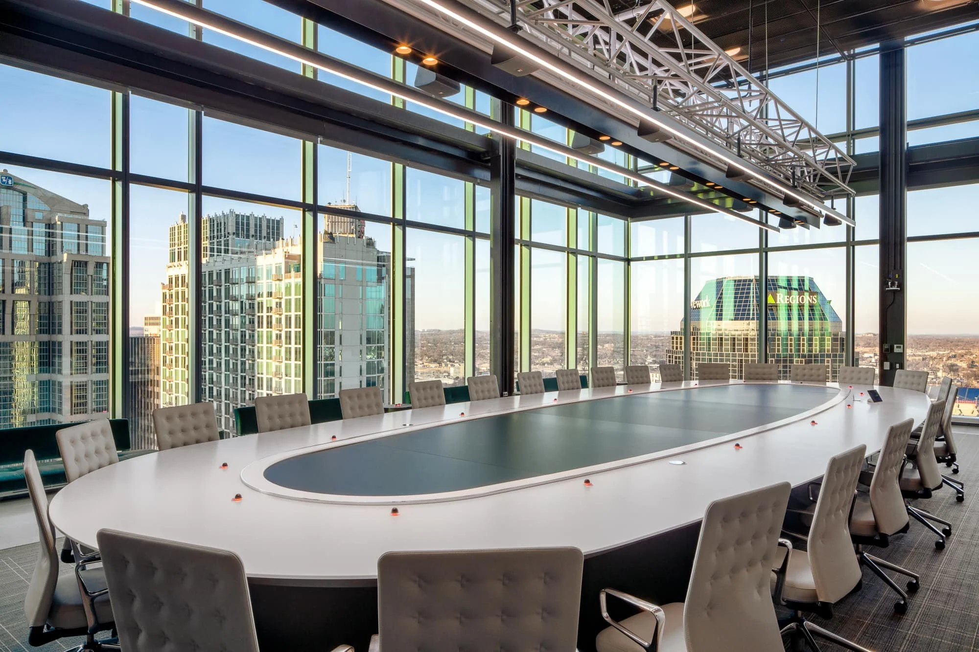 Alliance Bernstein Nashville executive boardroom with a large oval conference table, tufted chairs, exposed steel truss ceiling, and floor-to-ceiling glass overlooking the downtown skyline