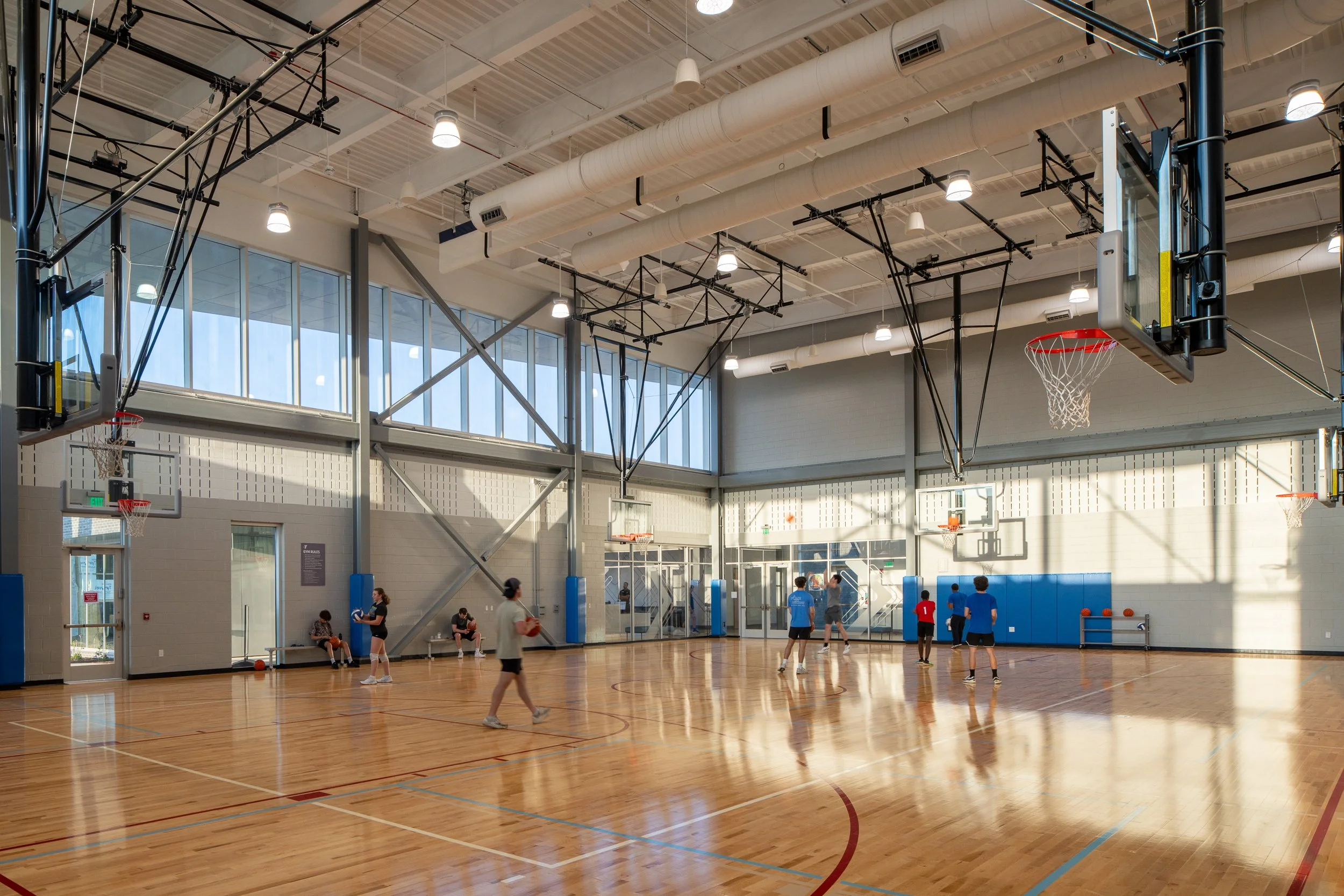 Players move through a sunlit gymnasium with blue column pads, glass walls and warm reflections on the court.