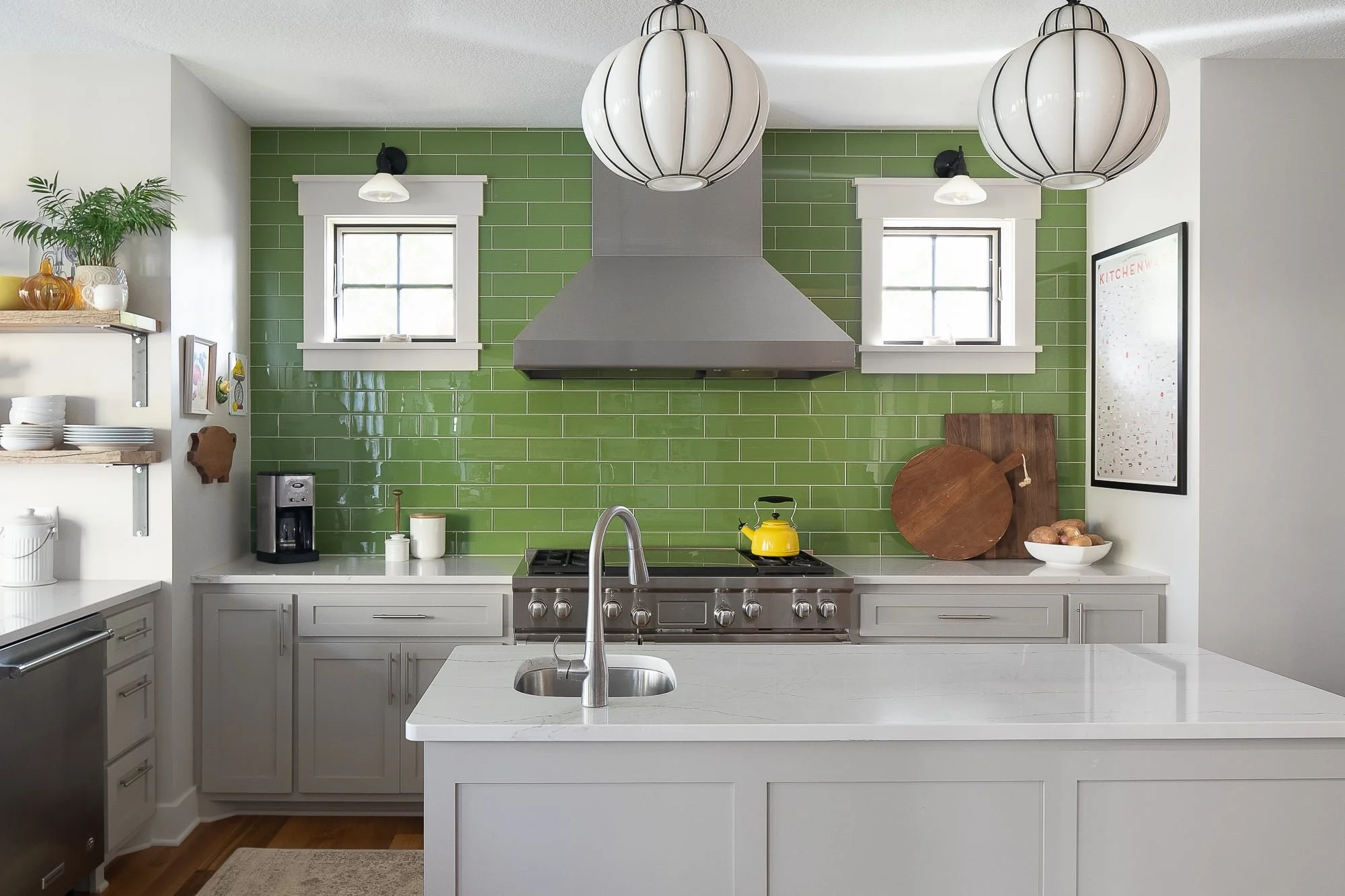 Bright residential kitchen with glossy green subway tile, gray cabinetry, a white island, pendant lights, and a stainless range hood.
