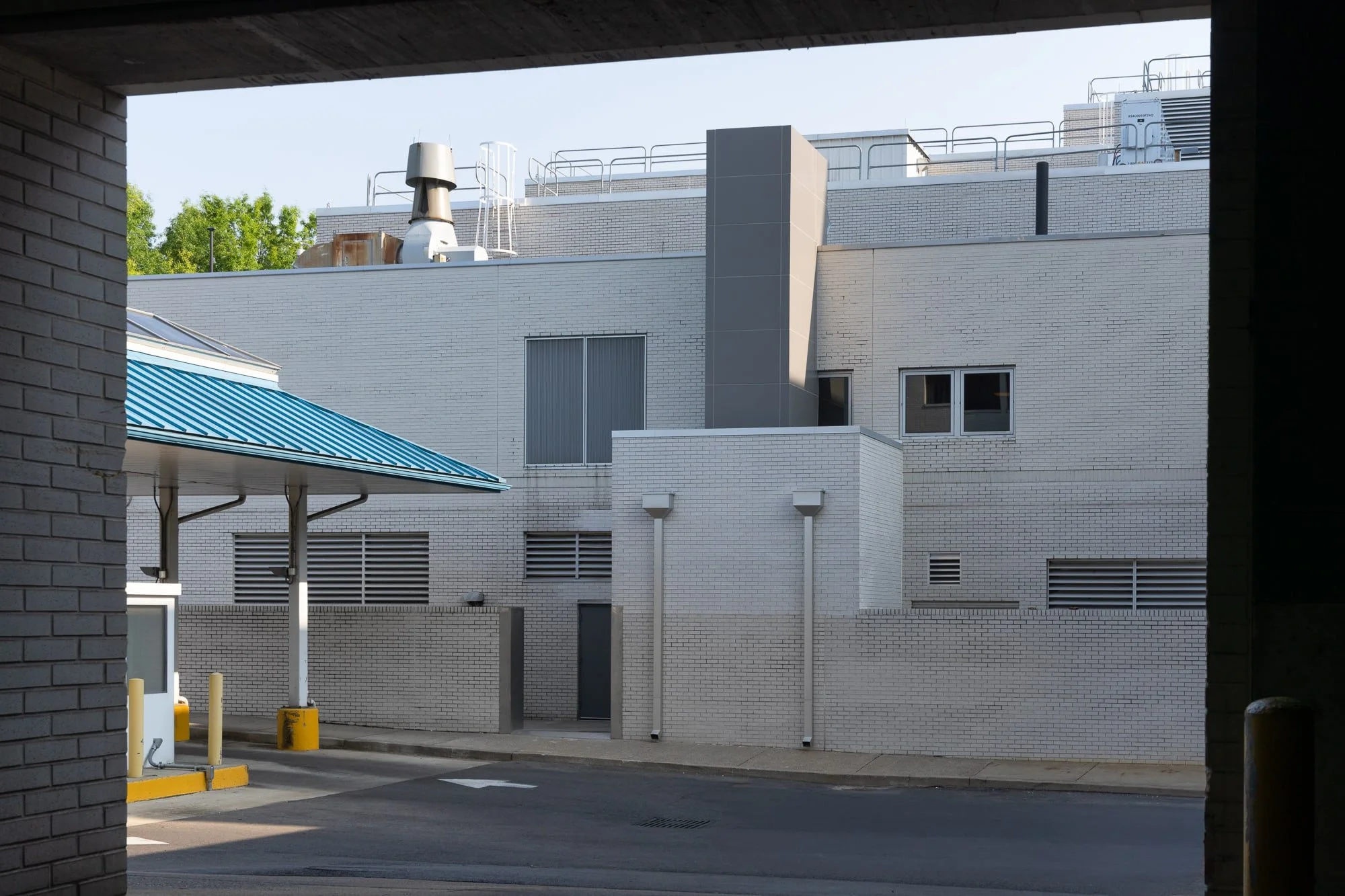 Exterior service area of a hospital building with white brick walls, rooftop mechanical equipment, vents, windows, and a covered drive-through lane.