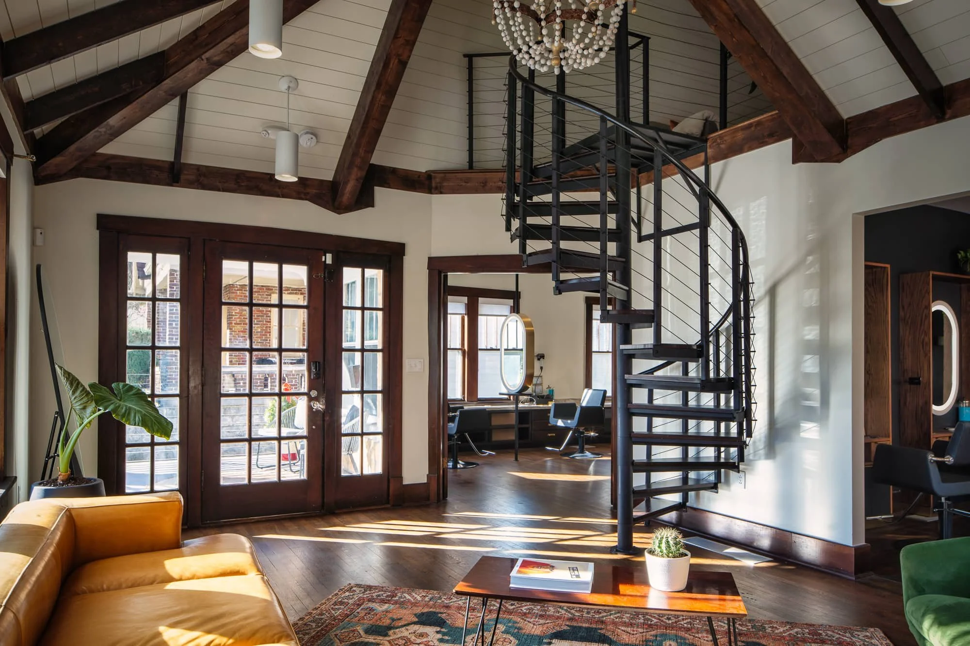 Rustic interior with exposed beams, spiral staircase, wood doors, and colorful lounge seating.