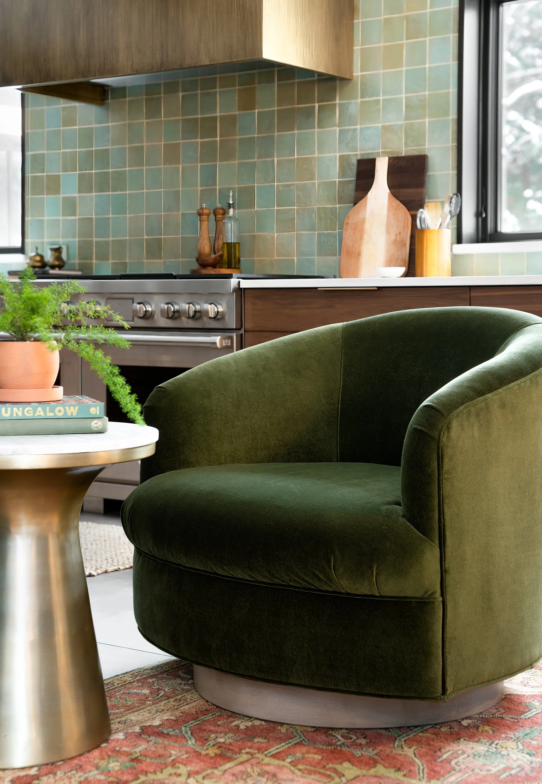 A cozy reading nook with a green chair and brass side table in a kitchen corner.