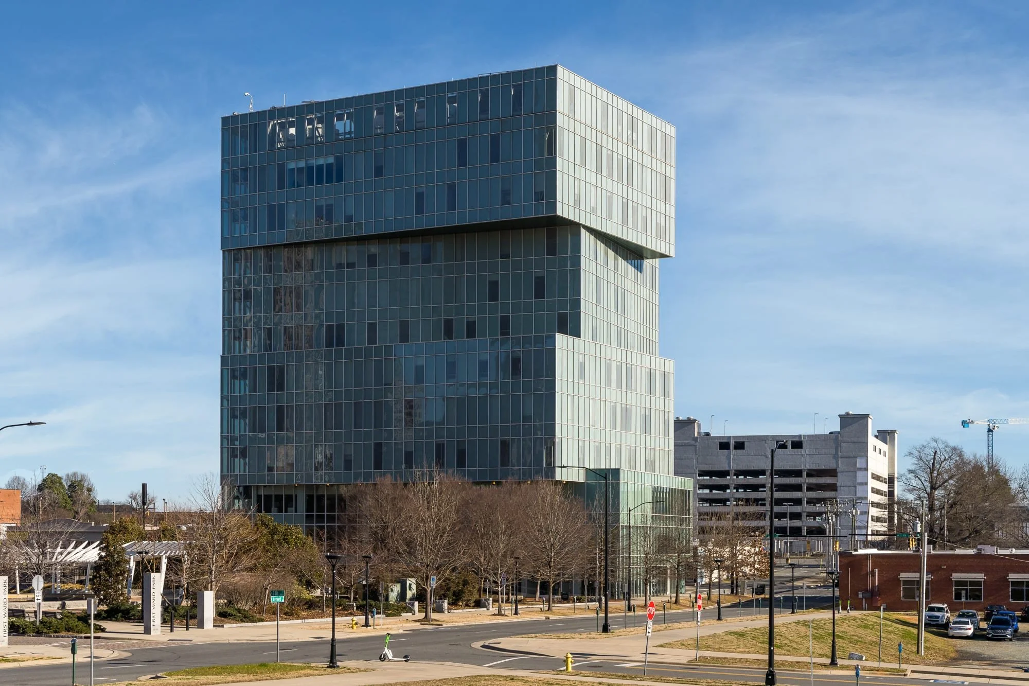 Tall glass tower beside First Ward Park with reflective windows and surrounding streetscape in downtown Charlotte.