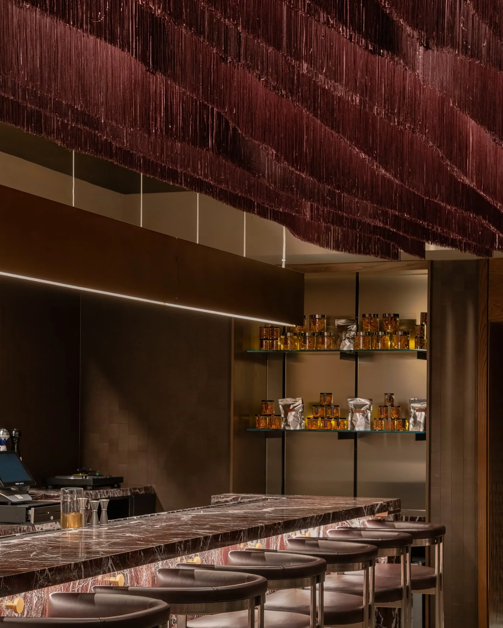 Detailed view of a burgundy suspended ceiling installation over marble bar seating and illuminated display shelves.