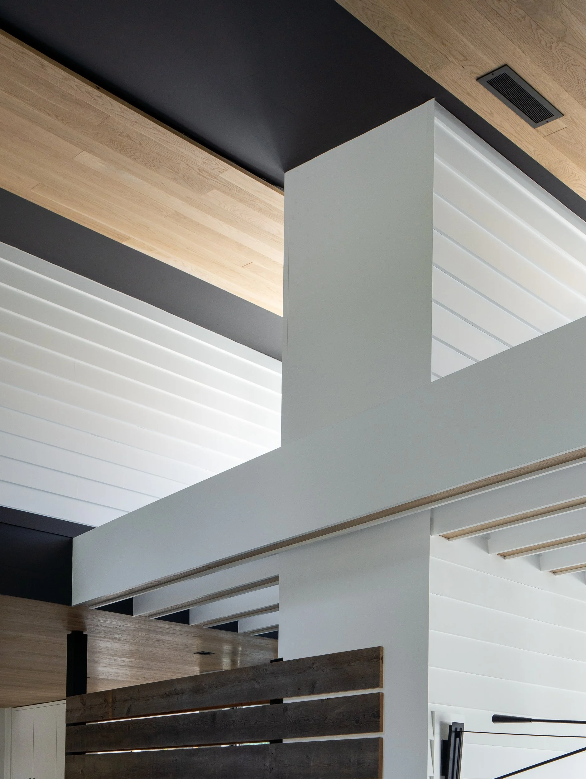 White interior walls rise toward high windows beneath a wood ceiling interrupted by dark structural elements.