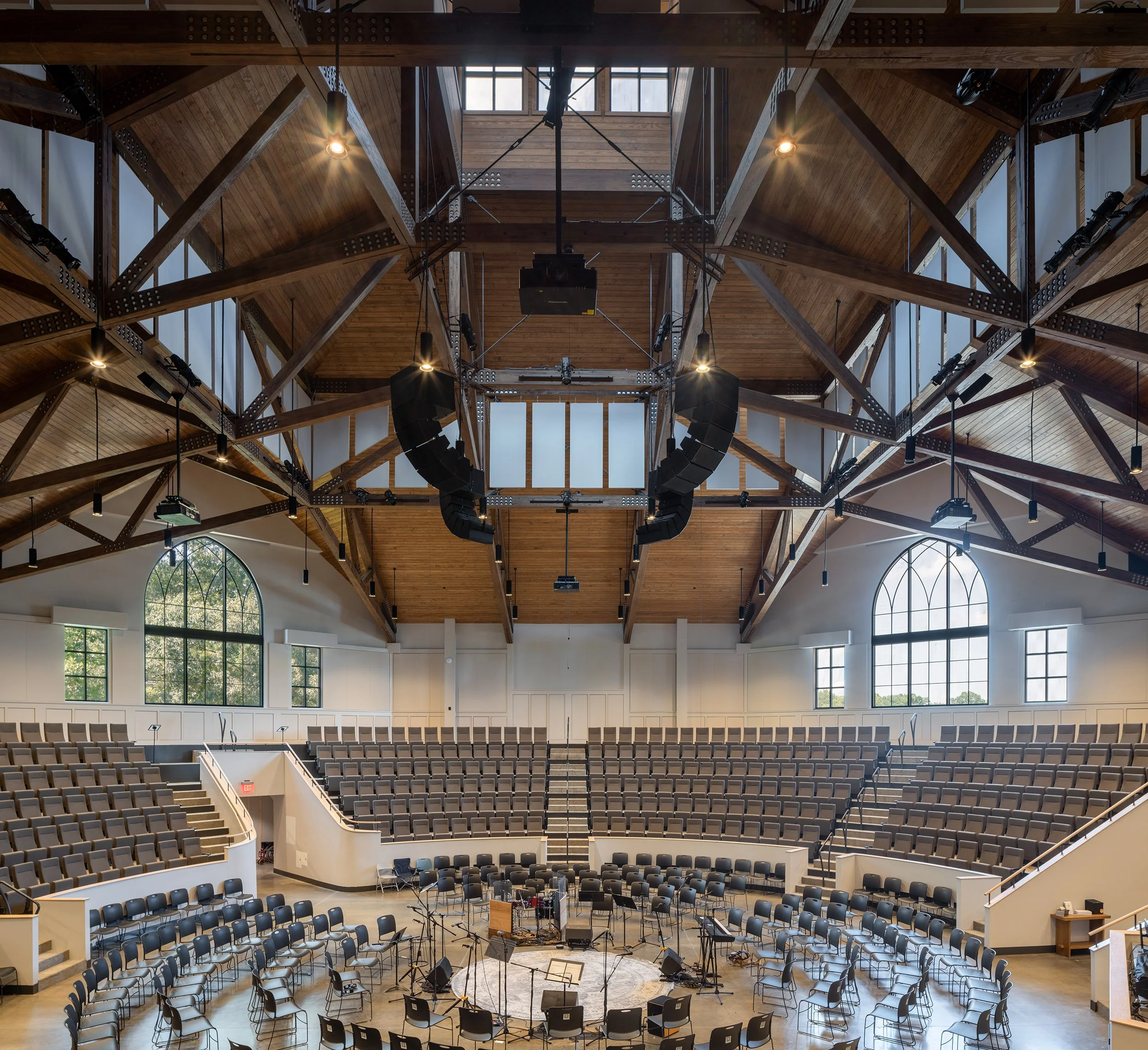 Sanctuary in the round at Storyhill Church in Davidson, NC with tiered seating, exposed heavy timber roof trusses, and gothic arched windows.